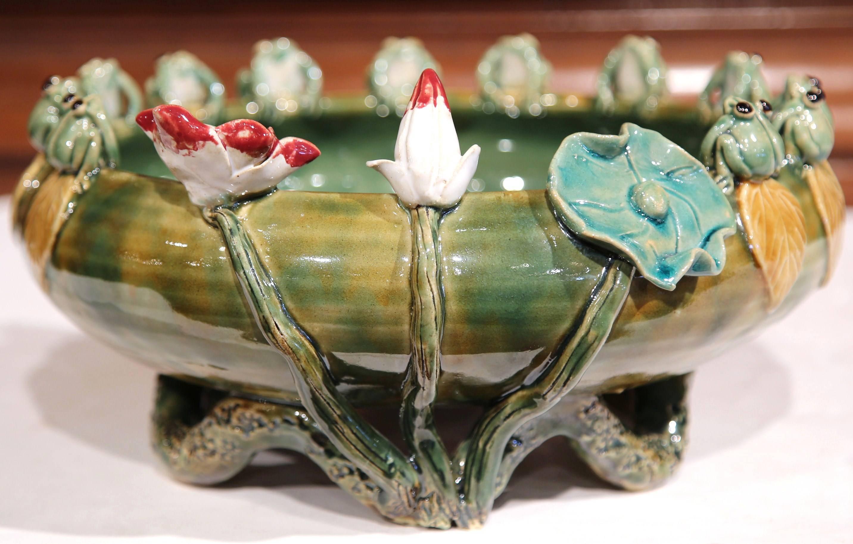 Bring a little color and charm to your home with this interesting Majolica bowl from France. The shallow, round green dish features a dozen frogs sitting on the rim. The porcelain jardinière is further decorated with a couple of flower stems and a