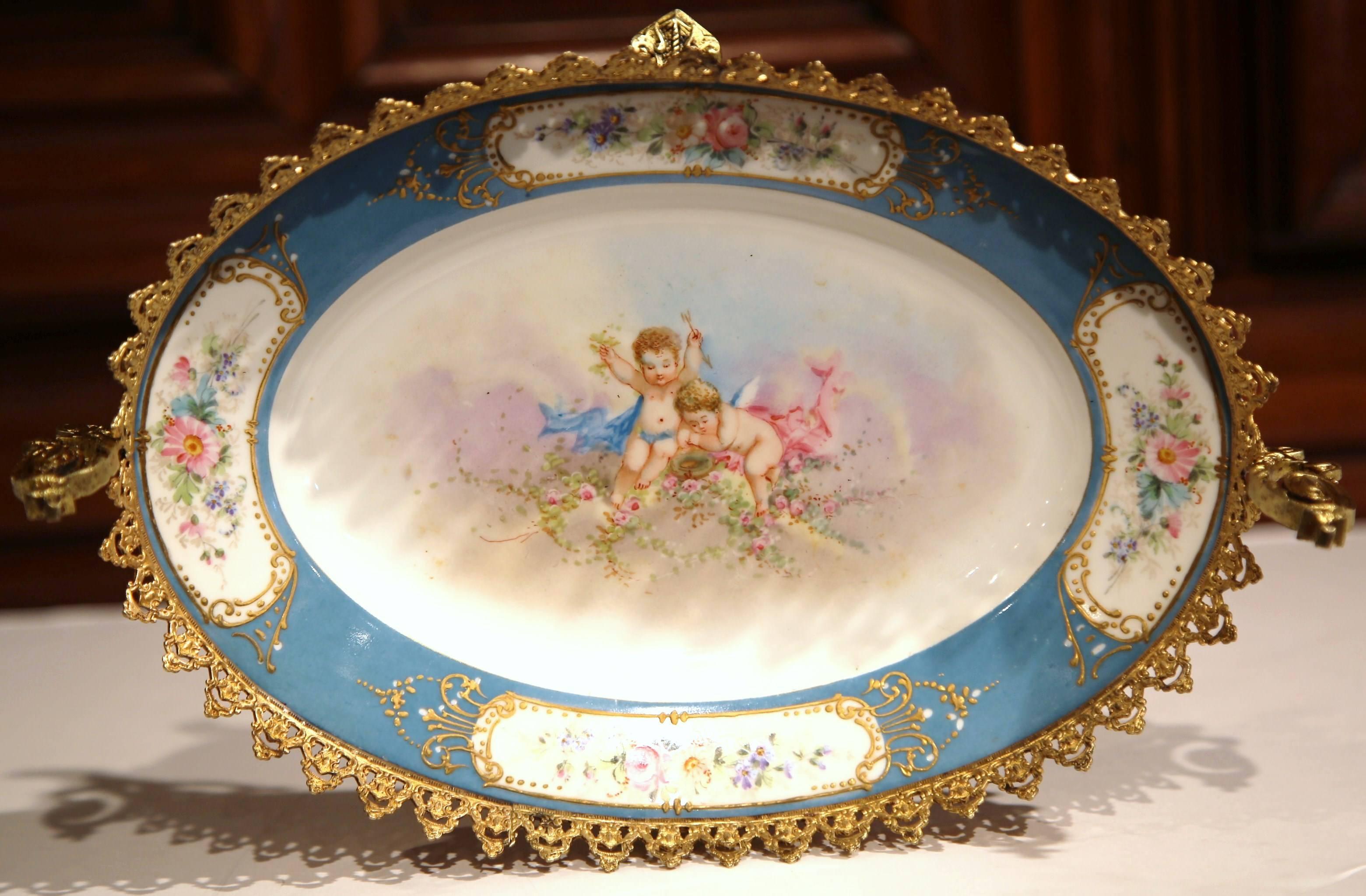 This elegant, antique blue and white vide poche was crafted in Sèvres, France circa 1870. The ornate decorative tray is embellished with hand-painted cherubs and flower medallions, as well as ornamental brass mounts, handles and scrolled feet.