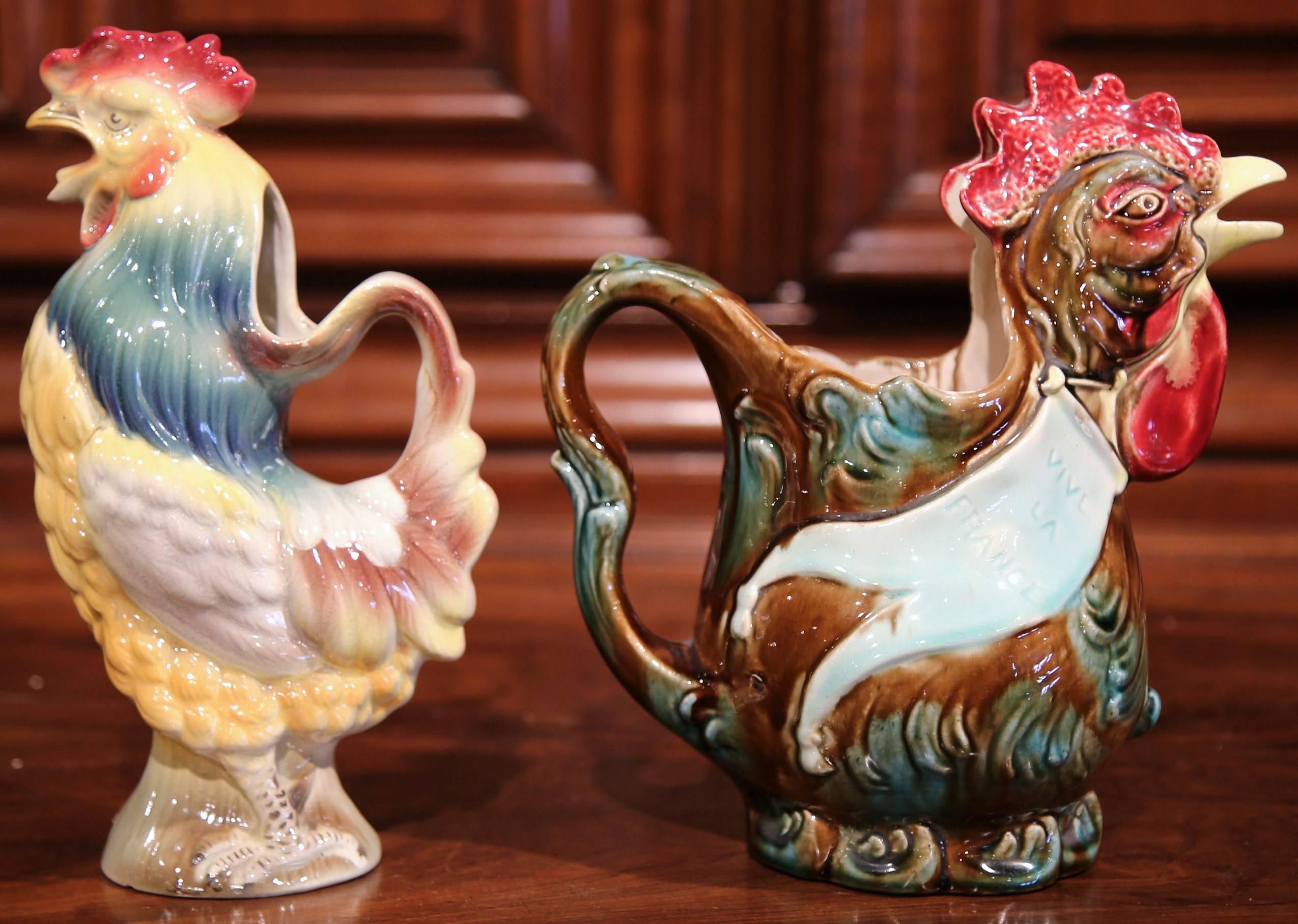 This set of two antique Majolica pitchers were sculpted in France, circa 1920. Each of the hand-painted, ceramic water jugs is in the shape of a colorful rooster with an open beak as a spout as well as a back handle for easy pouring. The larger