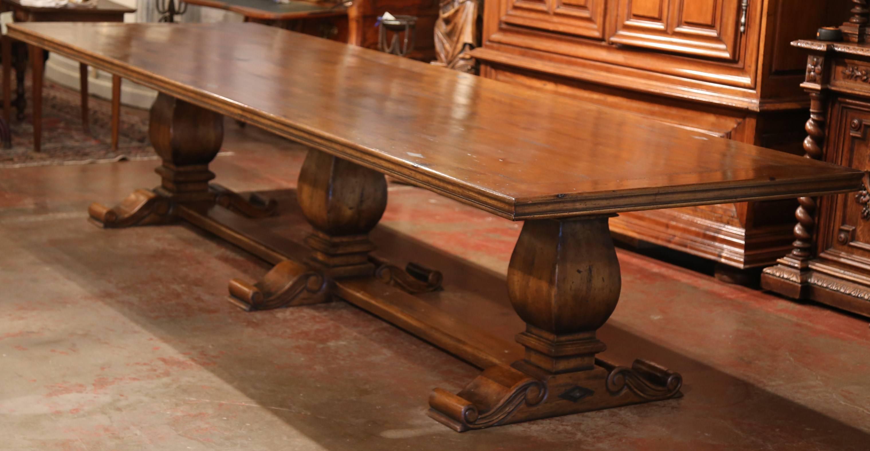 Fill a large dining room with this monumental farm table made from old walnut wood. The table is supported by three hand-carved 