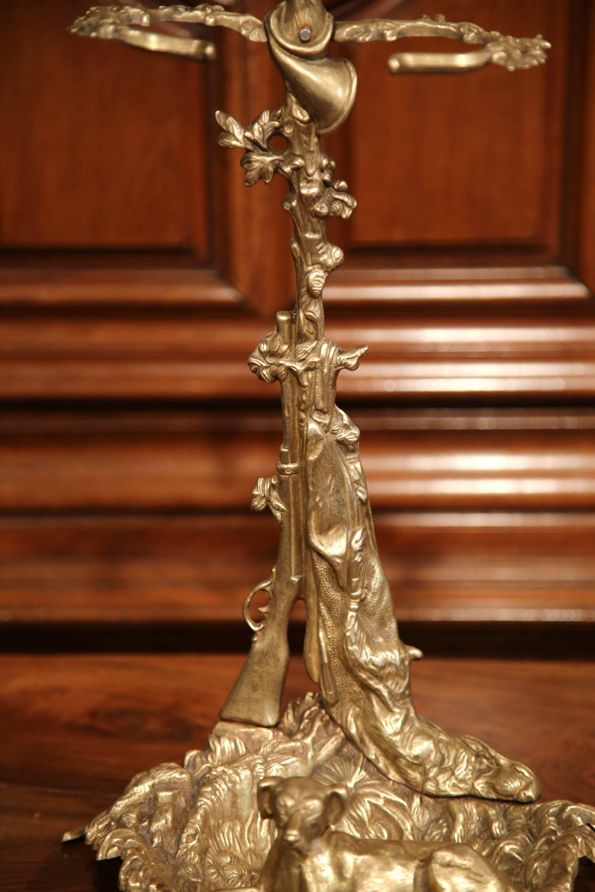 This fine antique umbrella or cane stand was crafted in France, circa 1870. The freestanding brass piece features a hunting theme that includes a gun, a rabbit, a horn and a dog motifs. The stand sits on four small feet shaped as leaves. The piece