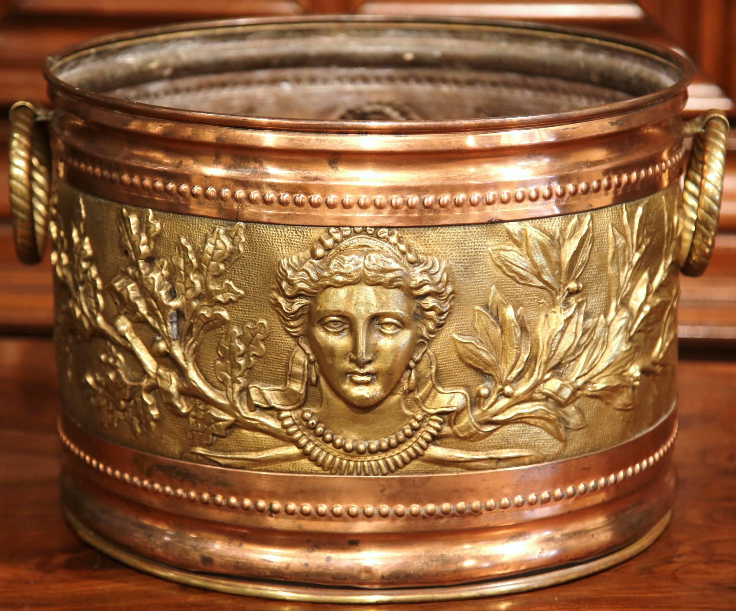 This large, antique planter was crafted in northern France, circa 1880. The round, brass and copper basket has two utilitarian rope side handles, and beautiful decorative repoussé motifs around the perimeter including detailed female faces and