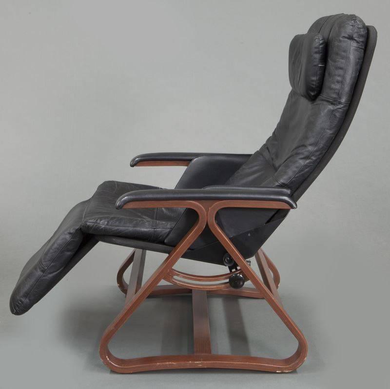 This comfortable and stylish reclining chair was made, circa 1980. The black leather seat has a headrest and is raised by triangular legs joined by stretchers. There are convenient knobs on both sides to adjust the chair angle to your ideal