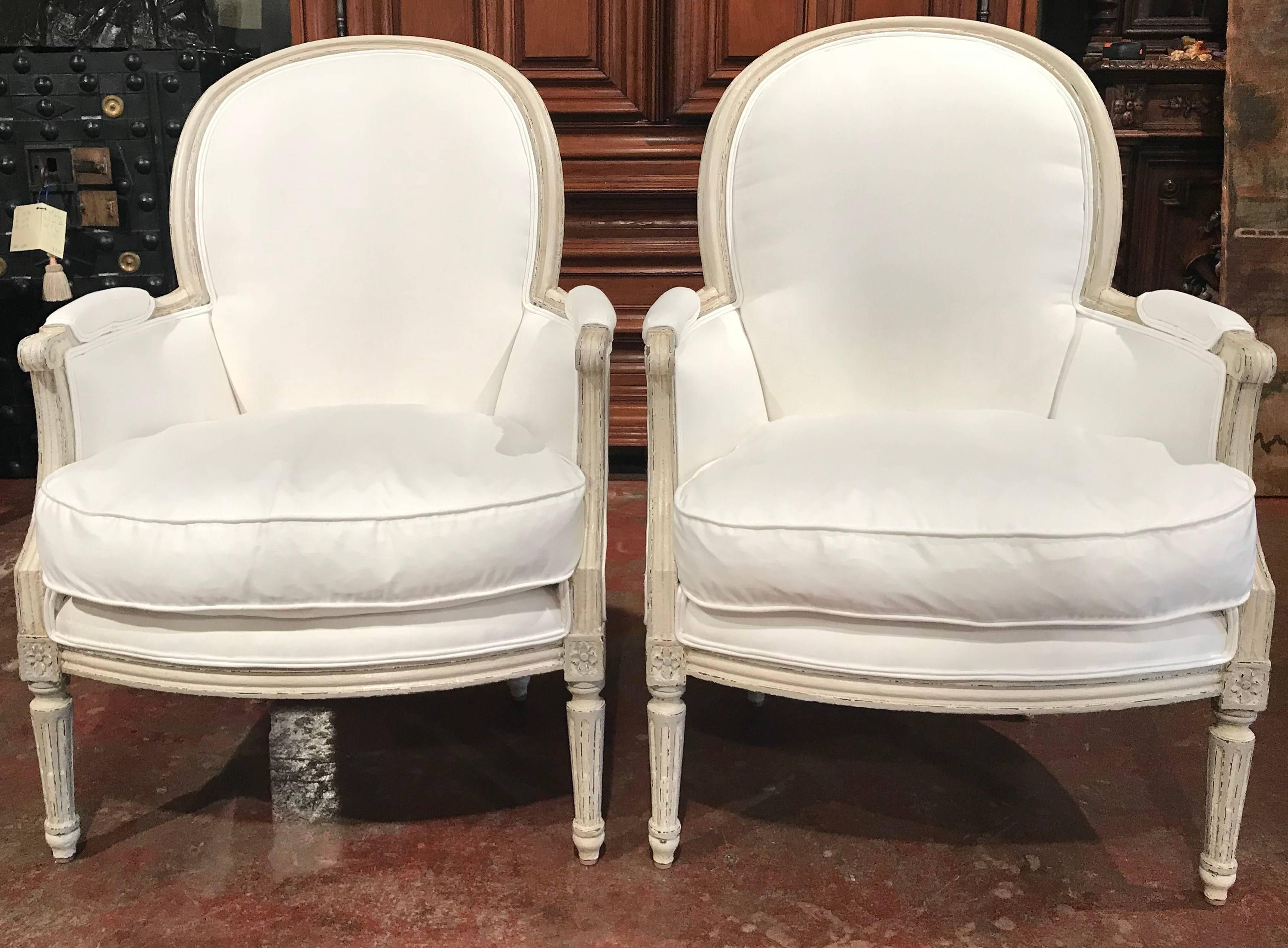 This elegant pair of painted bergeres was crafted in France, circa 1880. Each armchair features beautiful carved medallions designs above the tapered legs, two armrests and a curved and rounded back. The chairs are completed with comfortable down