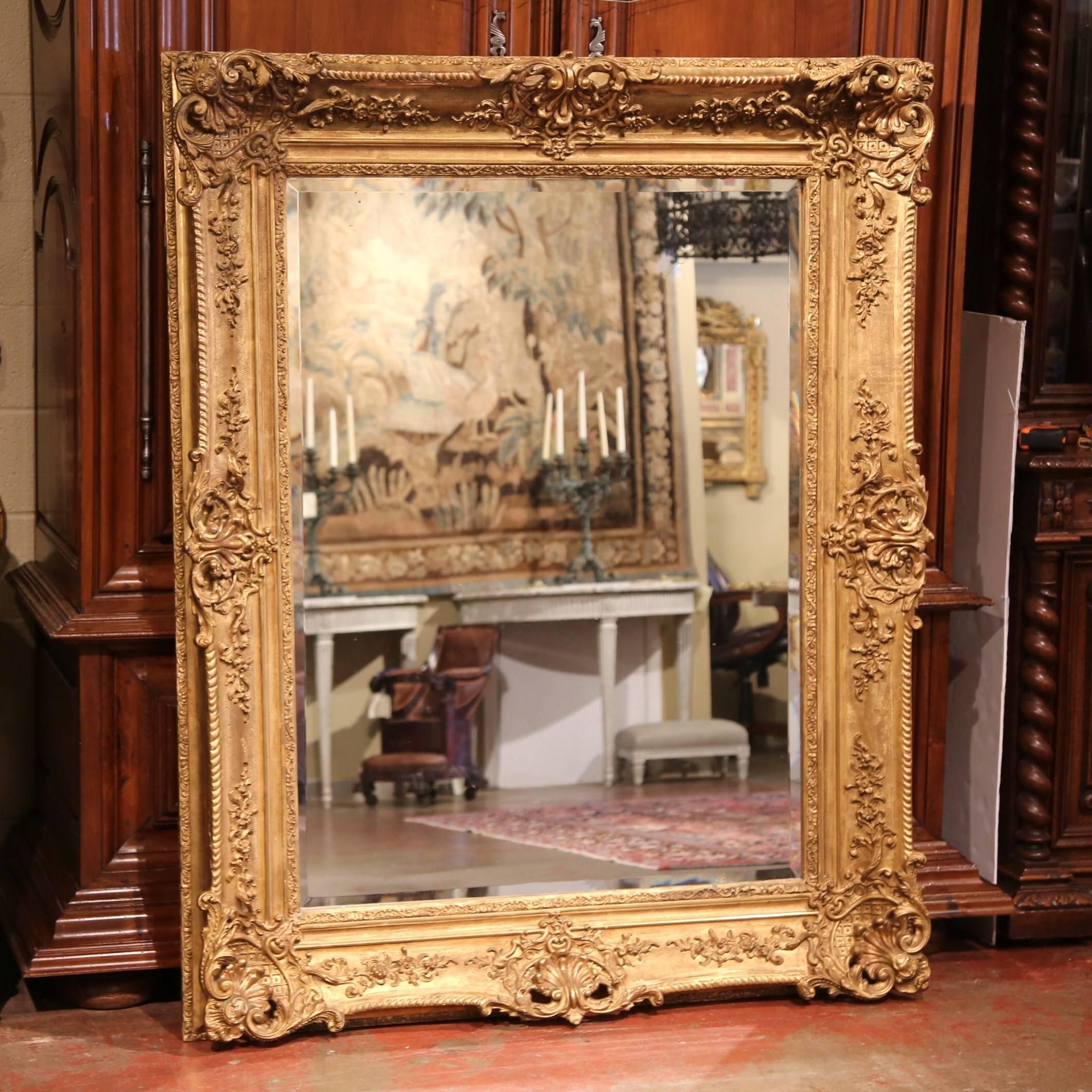 This elegant, antique mirror was created in France, circa 1860. Rectangular in shape, the large, gold leaf frame features exquisite carvings including floral decor, and is embellished with a cartouche shell motif in each corner. This stately mirror