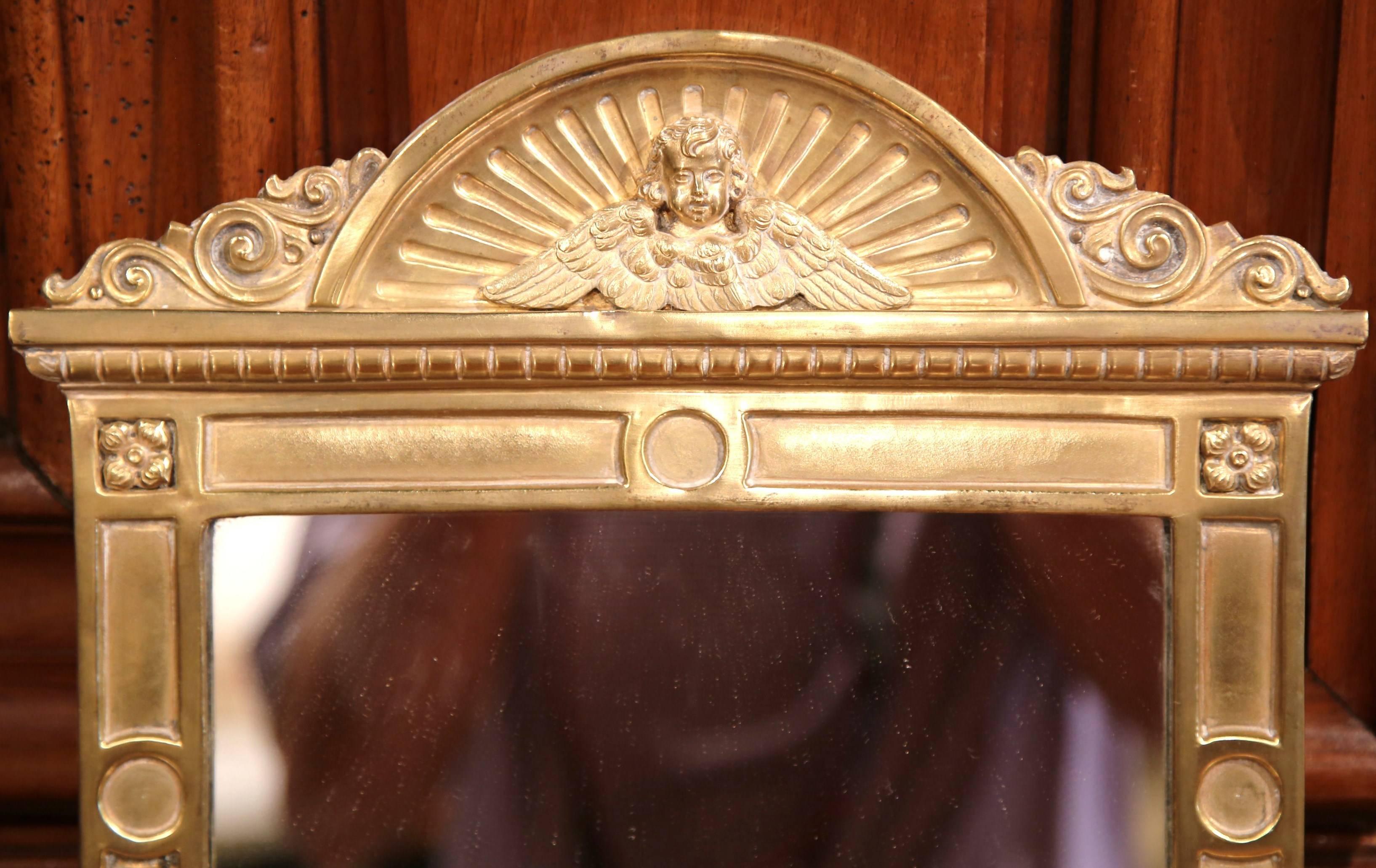 This small antique brass mirror was crafted in France, circa 1880. The wall hanging piece features intricate, repousse design, which includes an arched top with a center cherub and wings. There are two small round feet at the base and a Classic,