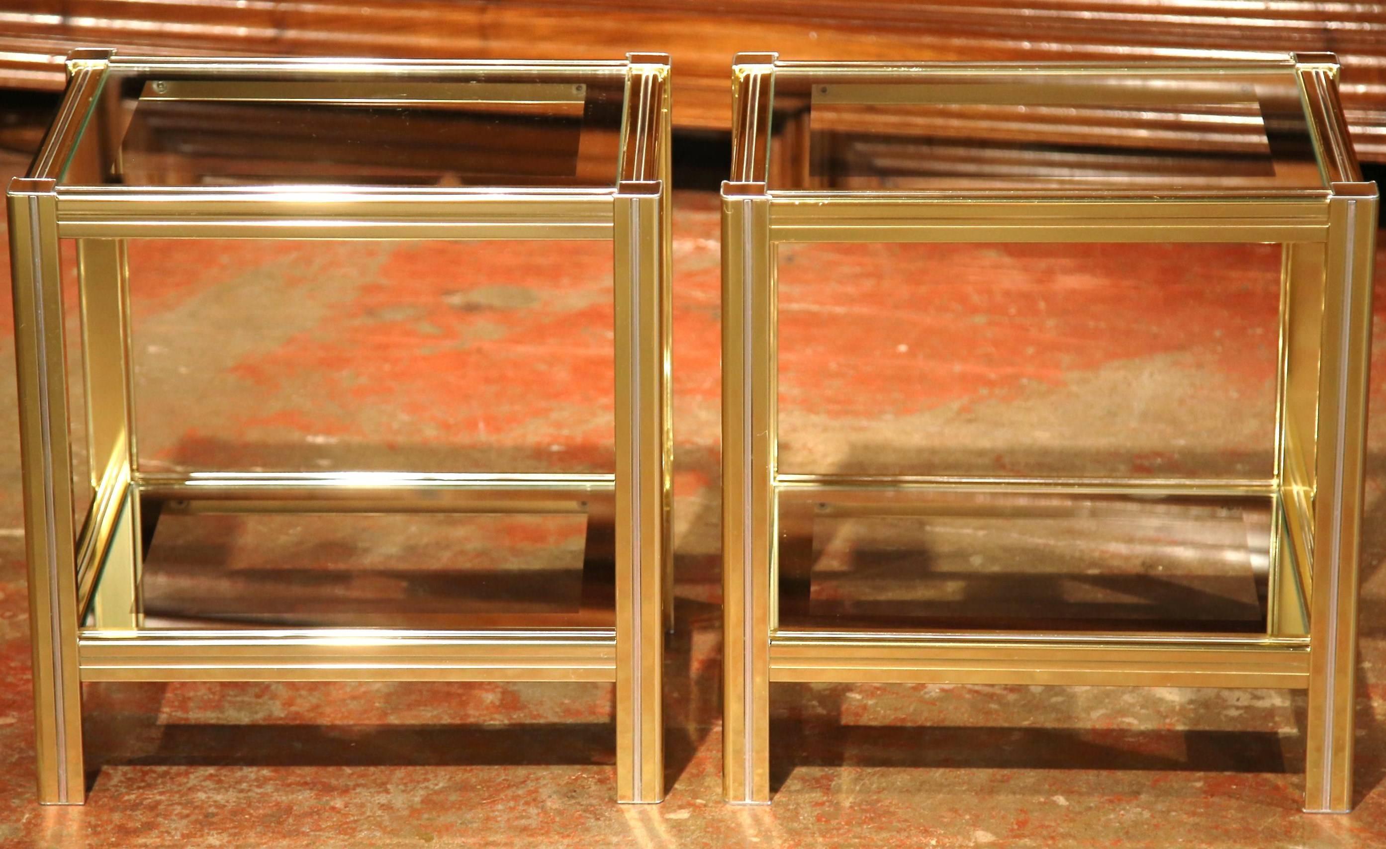 This elegant pair of vintage side tables was created in Paris, circa 1970. Each two-tier table has a chic, Minimalist style with square legs and a glass surface with gilt border on both top and bottom plateaux. The modern tables are in excellent
