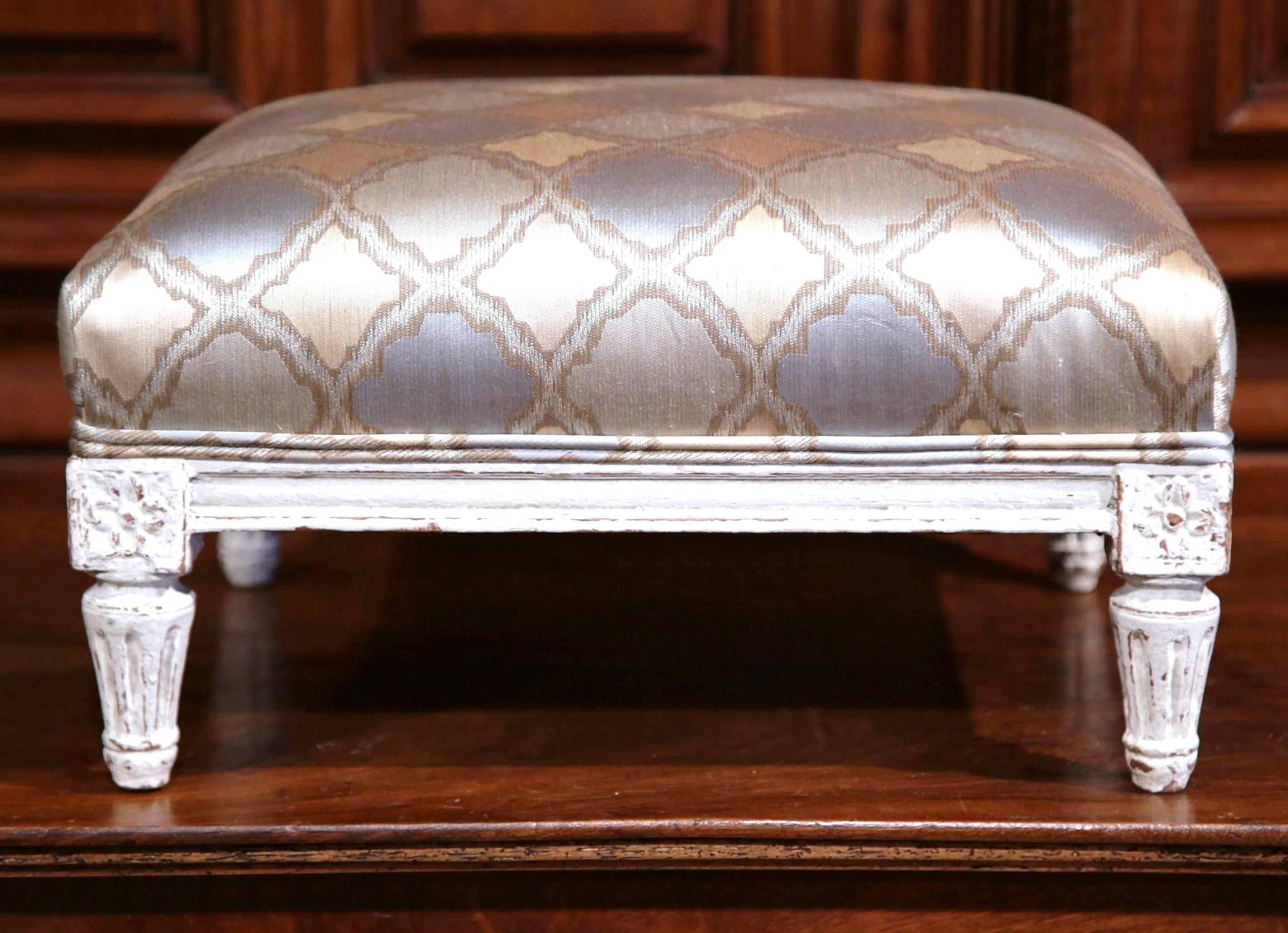 This large foot stool was created in northern France, circa 1890. The stool features tapered legs with hand carved square medallions. The footrest has a light gray antique rubbed painted finish and has been reupholstered with a pale blue and beige