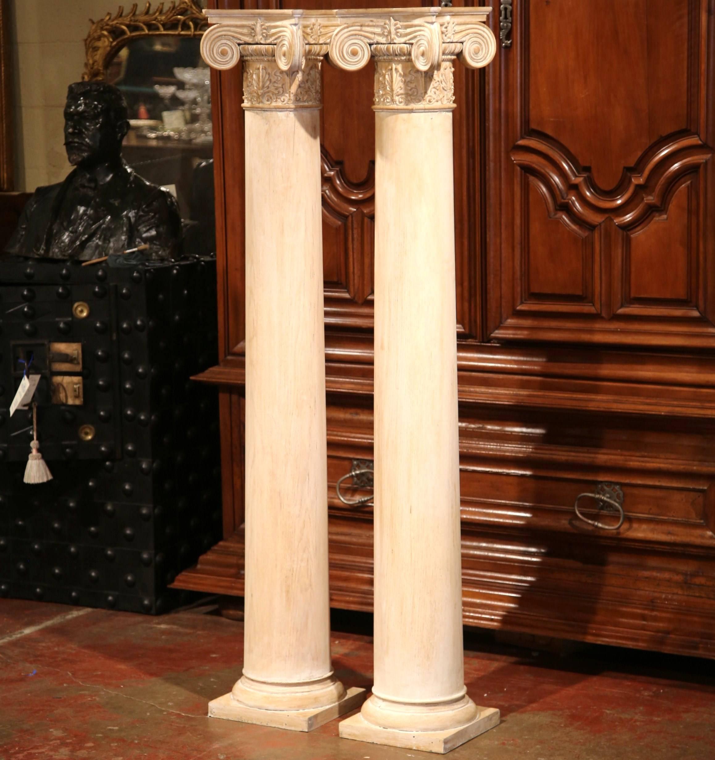 Elegant pair of antique columns from France; crafted circa 1860, each tall column features a square top with hand-carved fleurs de lys and large scrolls at each corner, a round stem and square base at the bottom. The pedestals are in excellent