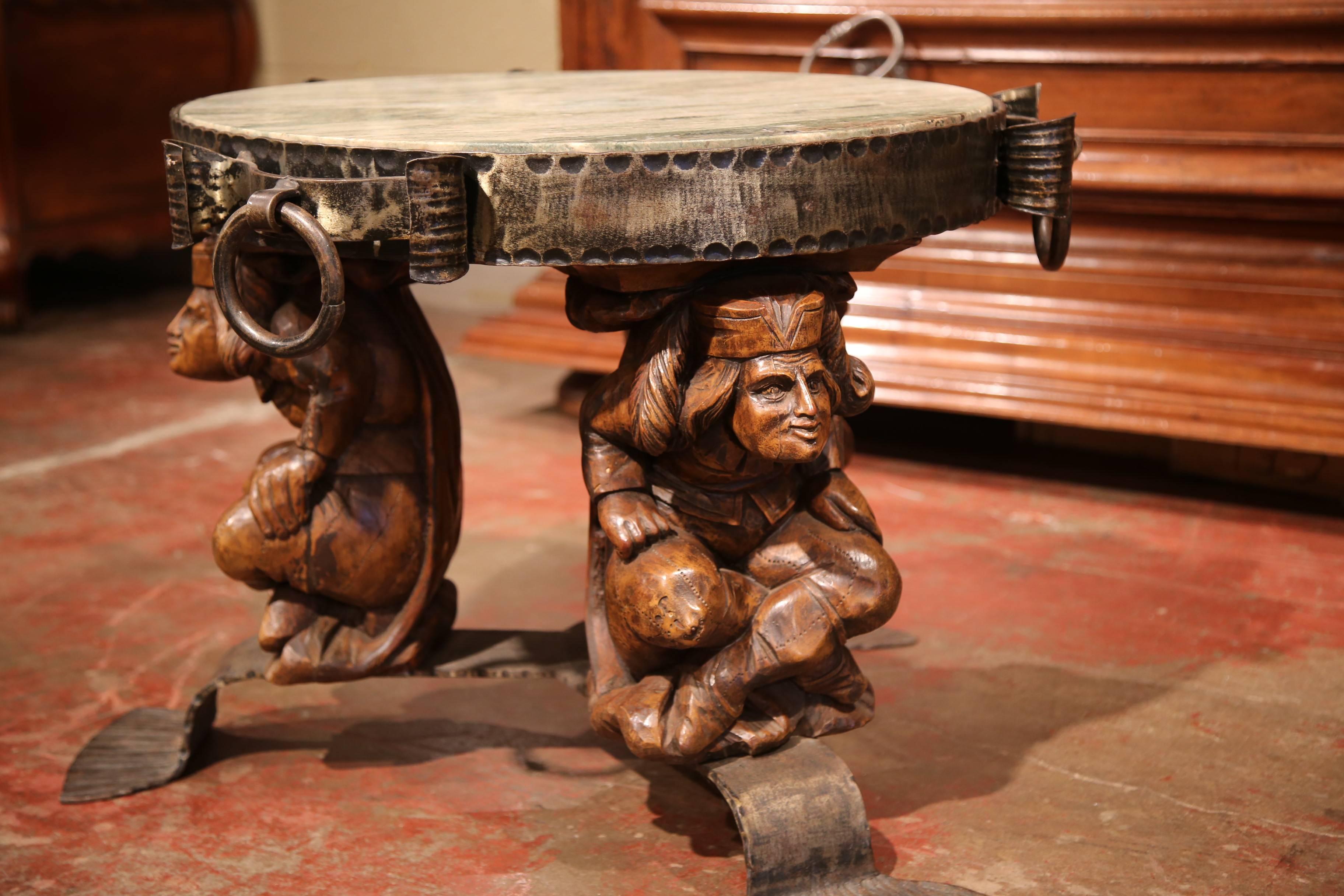 This interesting Gothic coffee table was crafted in southern France, circa 1880. The antique cocktail table features three carved renaissance male figures sitting on iron feet holding a round gray and green marble top. The piece has a forged rim