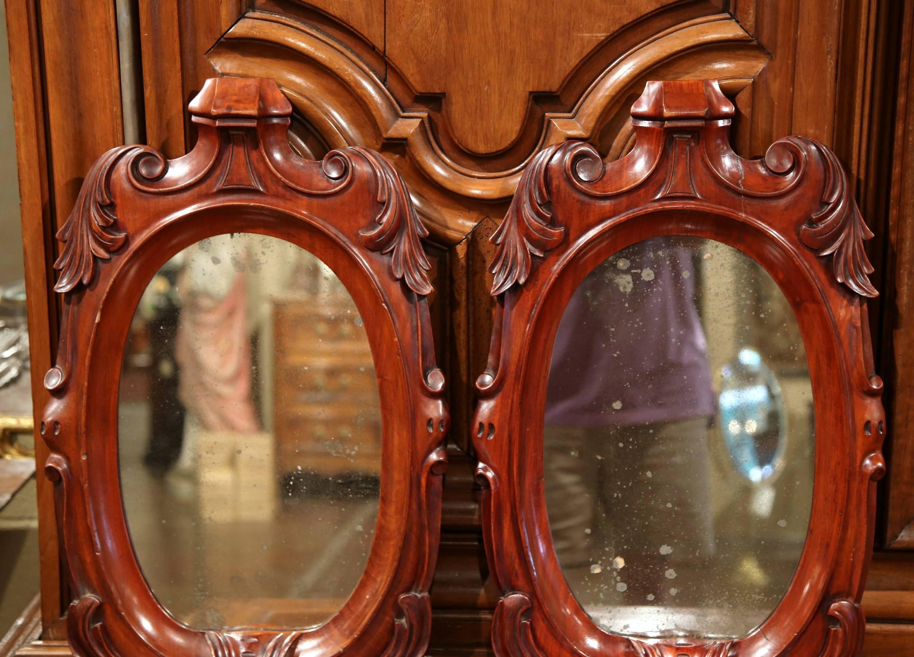 These elegant antique wall hanging mirrors were crafted in France, circa 1890. Each fruit wood mirror features hand carved foliage decor in high relief and the original oval mercury glass. The mirrors are in excellent condition, and the ornate
