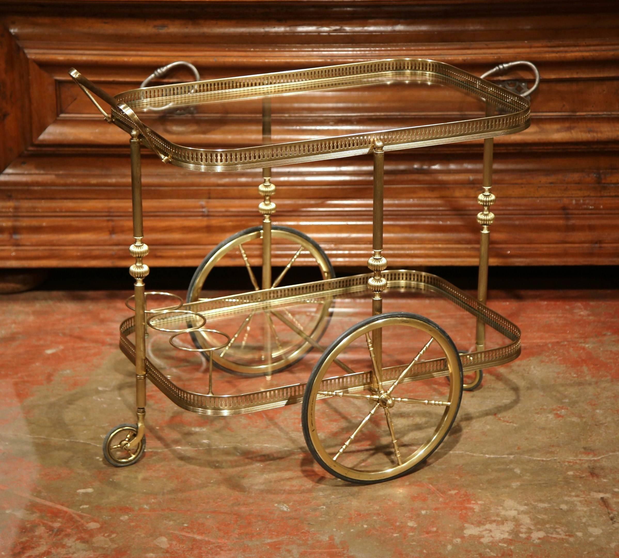 Store your liquors elegantly with this vintage bar cart. Created in France, circa 1920, the bar cart has two tiers and is set on top of two large wheels and two smaller ones for easy movement. The table has a large handle with brass gallery tray on