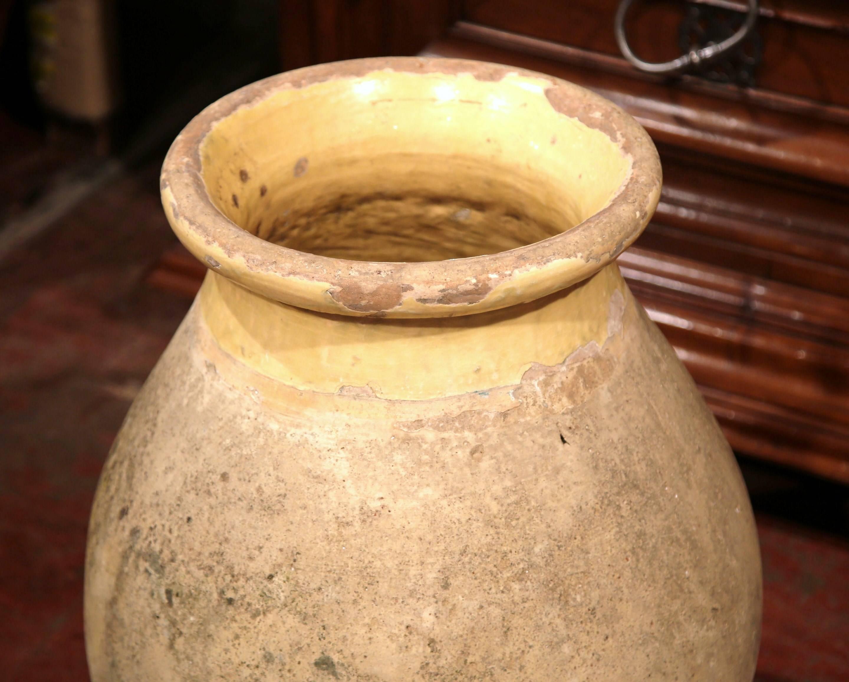 This beautiful, antique earthenware olive jar was created in southern France, circa 1880. The jar has a traditional round shape and a gracefully handmade quality. The large pot has a neutral, yellow glaze around the neck and trim, and a natural