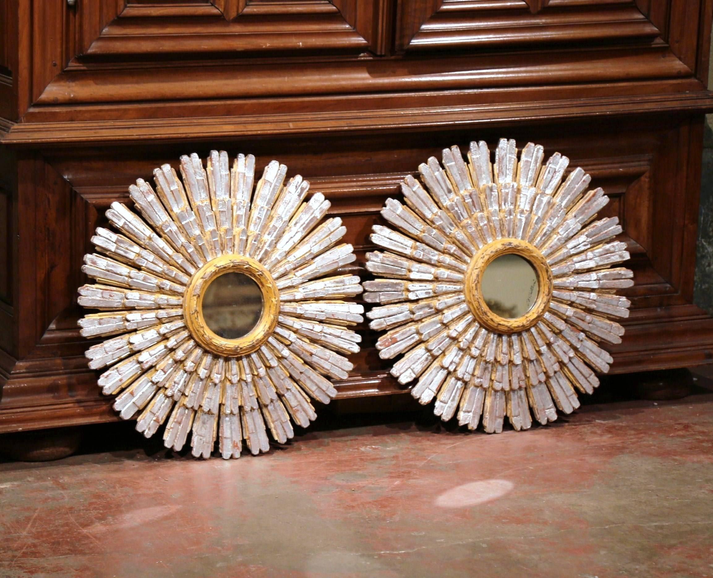 This large pair of vintage sunburst mirrors were carved and painted in France, circa 1940. Each ornate wall hanging mirror features a small round center glass with a two-tone paint finish. The sun rays shooting out from the central mirror are very