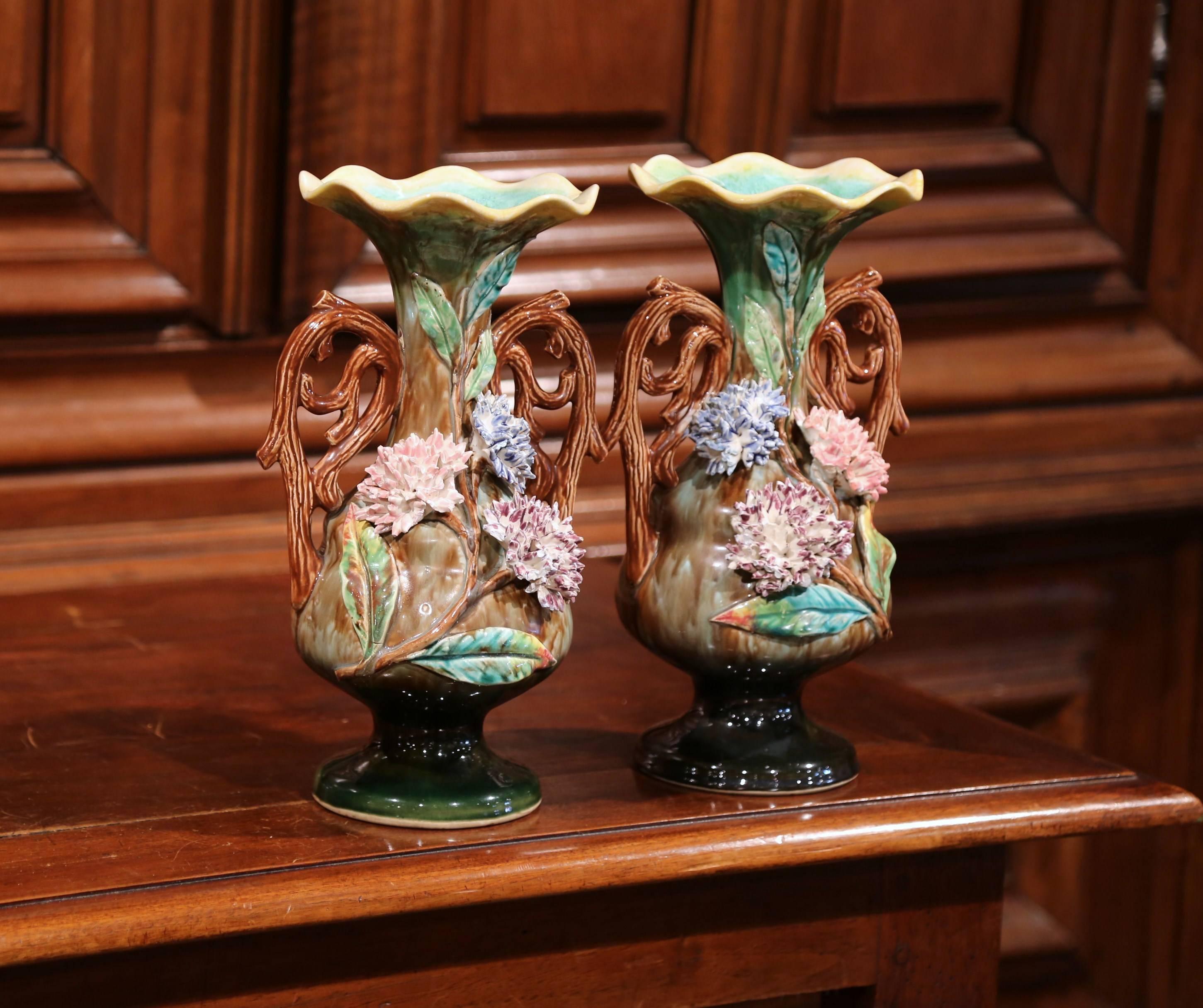 This colorful pair of antique Majolica vases were crafted in France, circa 1880. Each artful vase features hand-painted hydrangea flowers, stems and leaves in a realistic high relief shape. The vases have handles shaped like plant roots and are in
