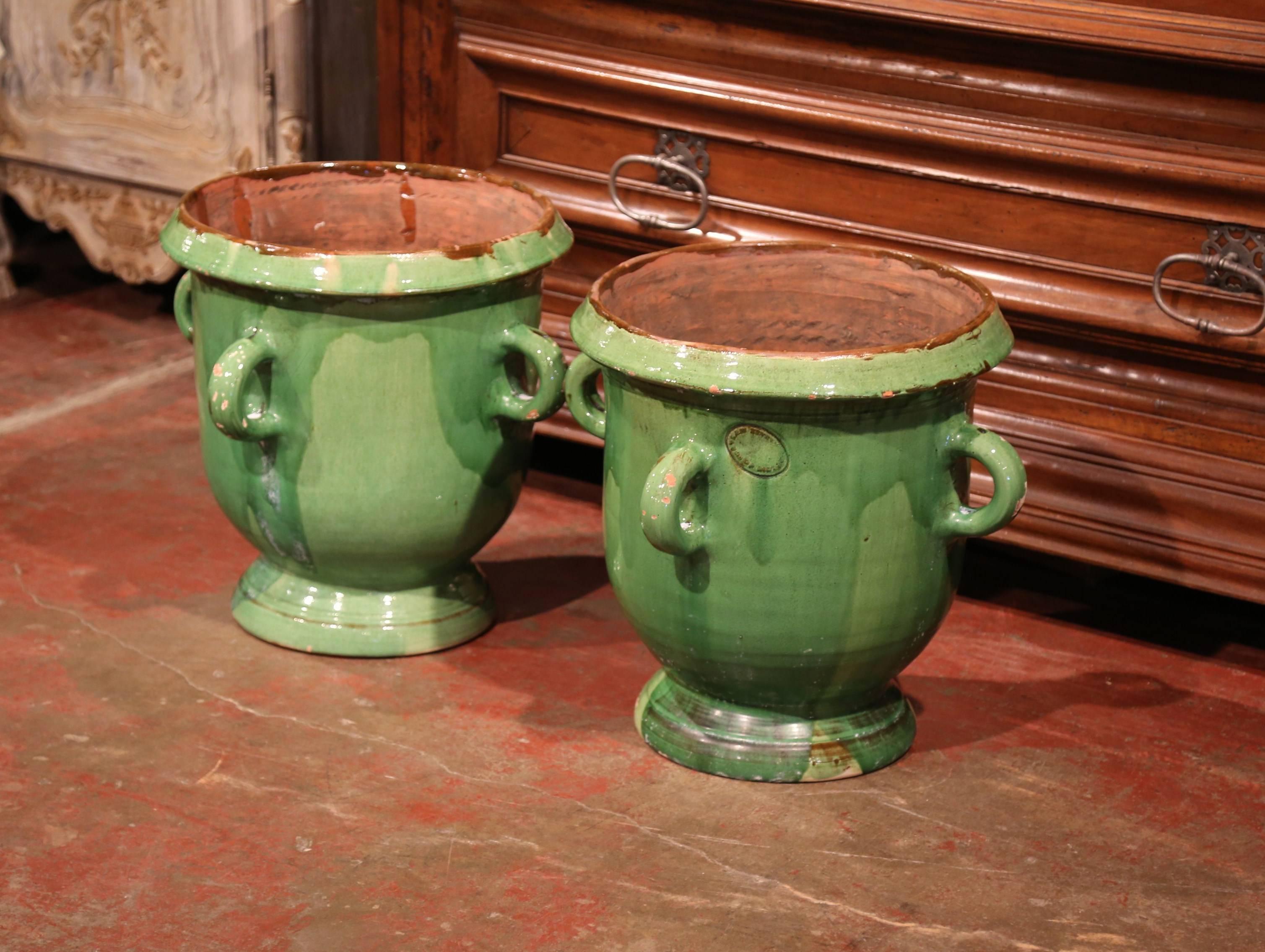 This large, colorful pair of terracotta pots was created near Anduze, France circa 1960. Each classic earthenware planter has four handles and has been recovered with a glazed Provençal green finish. The pots are in excellent condition with a rich