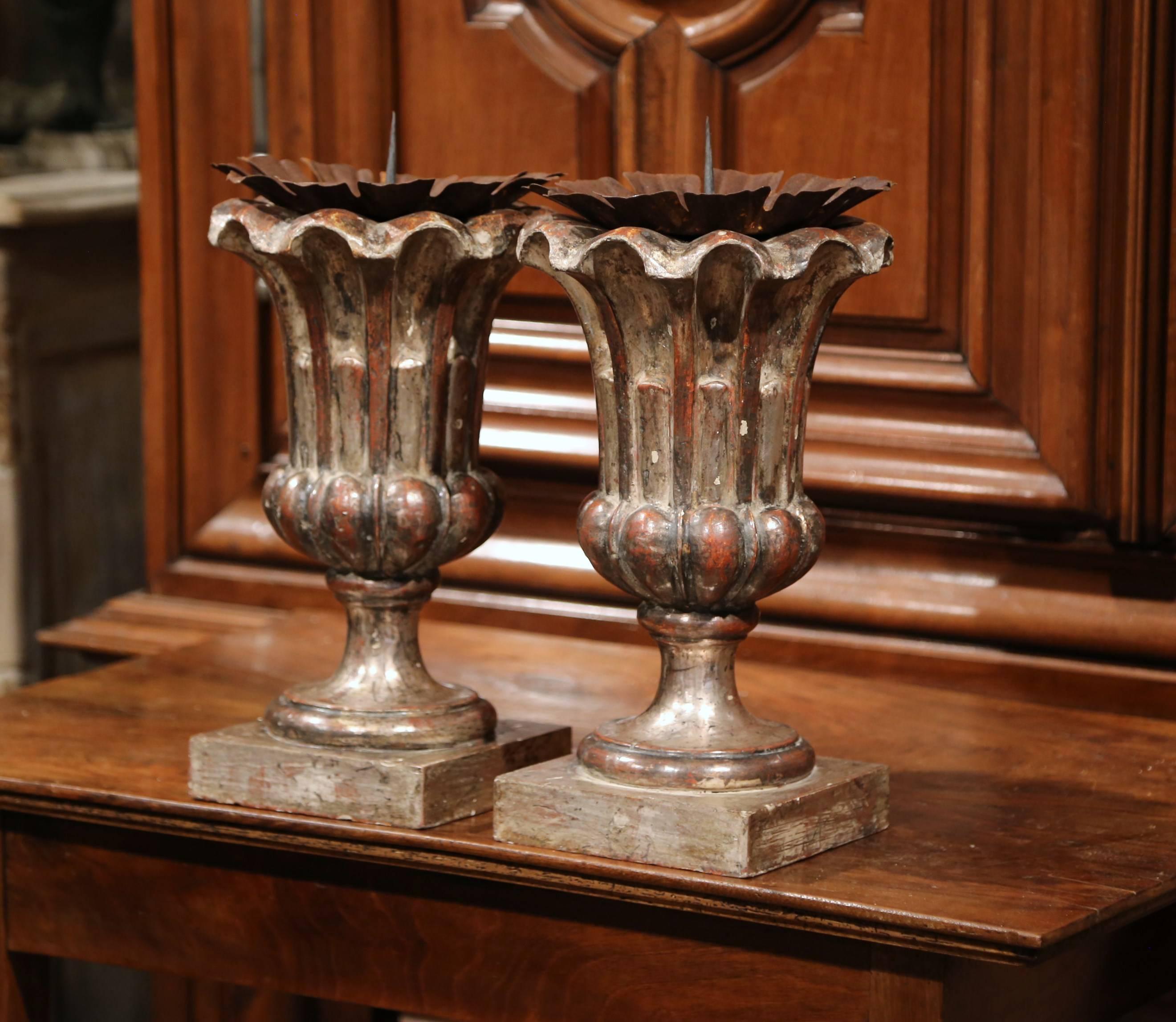 This elegant pair of ornate candlesticks were carved in Italy. Both pieces have a dramatic, Baroque shape and are coated with a metallic silver leaf finish. These prickets have metal plates to catch melting wax, and could also be mounted into