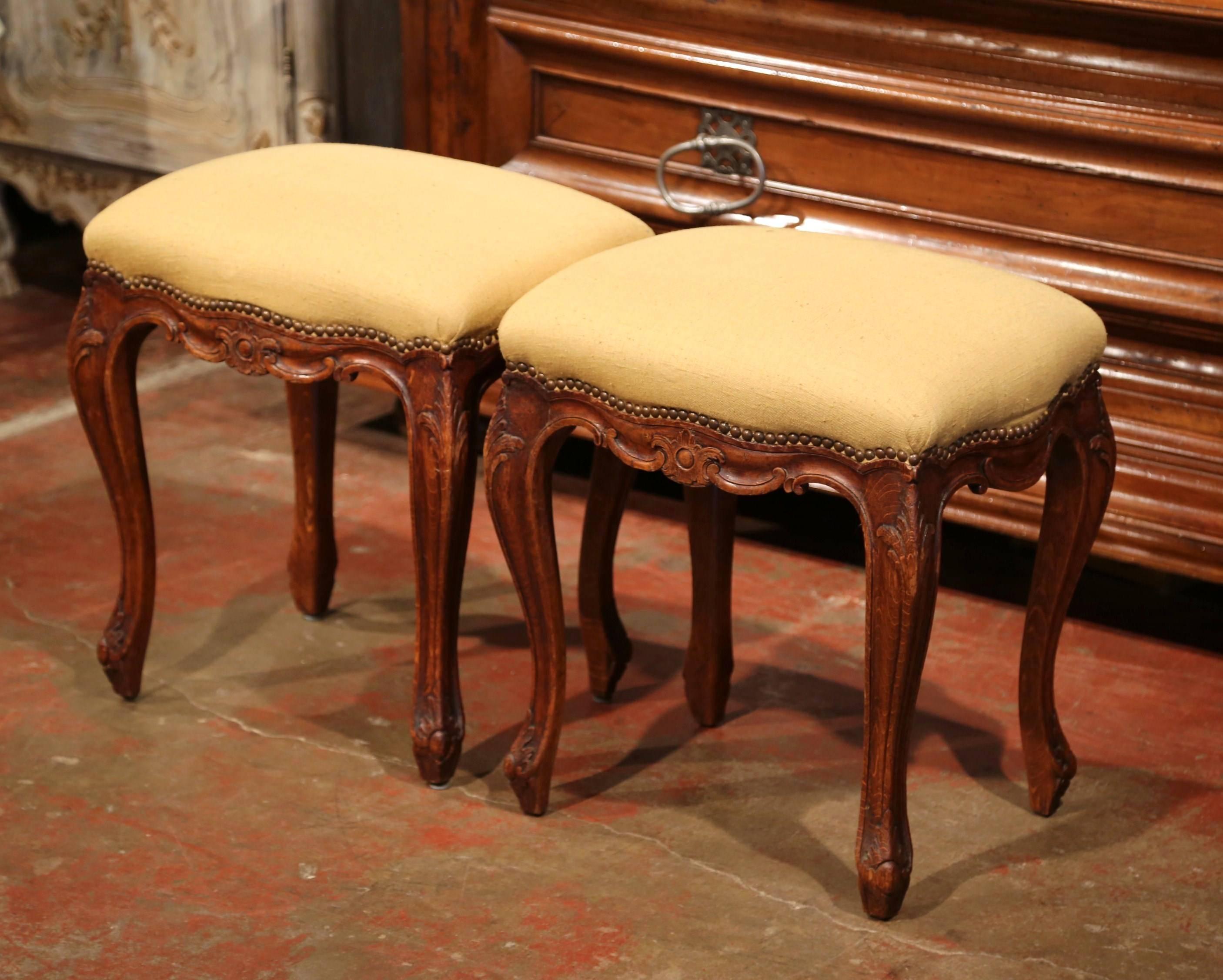 Elegant pair of antique stools from Normandy, France; crafted circa 1920, the seating pieces features fine carvings around the curved and shaped apron, four cabriole legs with acanthus leaves over the feet. The hand carved stools are upholstered