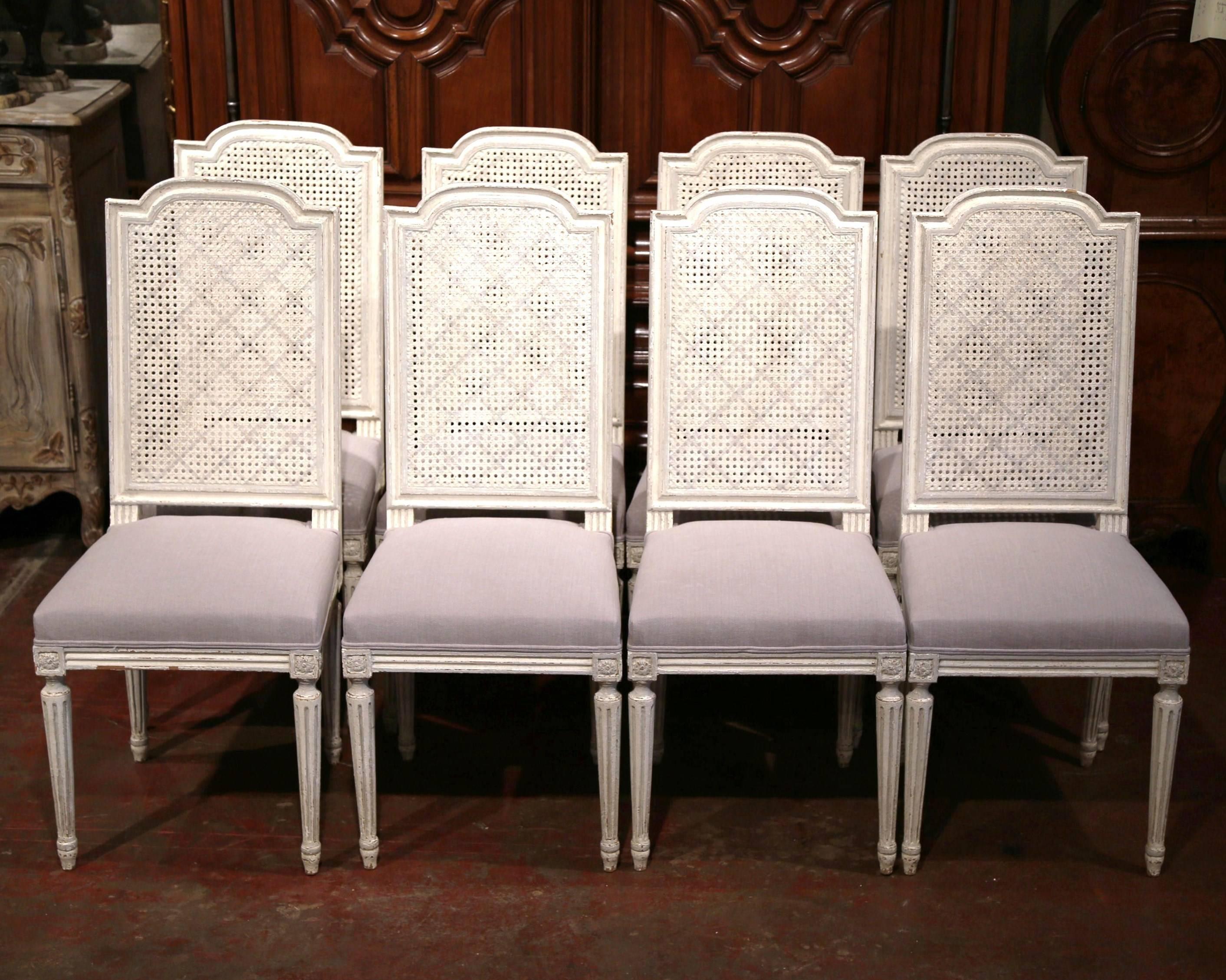 This elegant set of antique painted dining room chairs was crafted in France, circa 1900. Each side chair features a tall rounded back with cane work, an new upholstered seat with grey fabric and four fluted legs with carved medallions at the