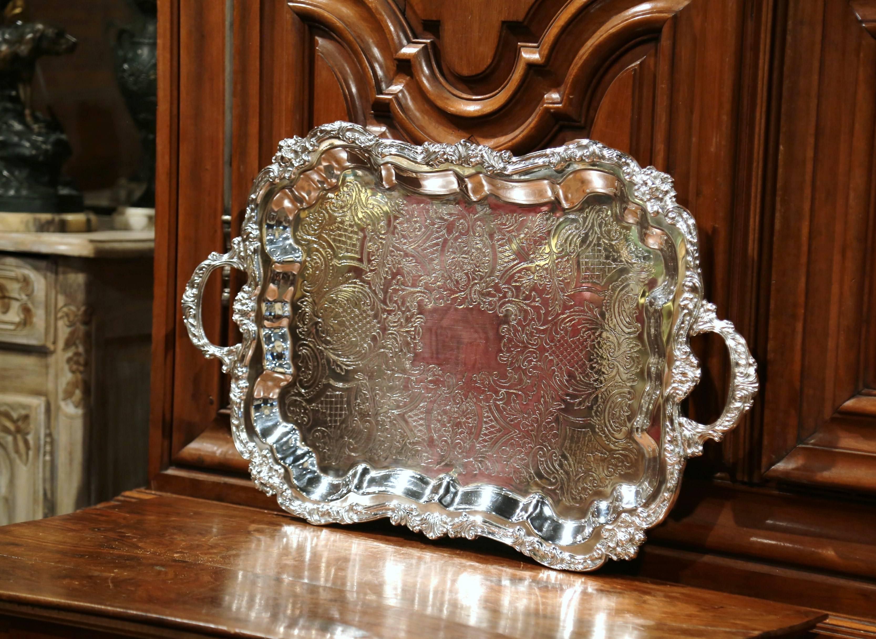 Elegant antique silver plated tray from France, crafted circa 1920, the decorative tray sits on four curved feet and features ornate handles on the sides, elaborate scrolls around the perimeter and engraved decor on the surface top. The piece is in