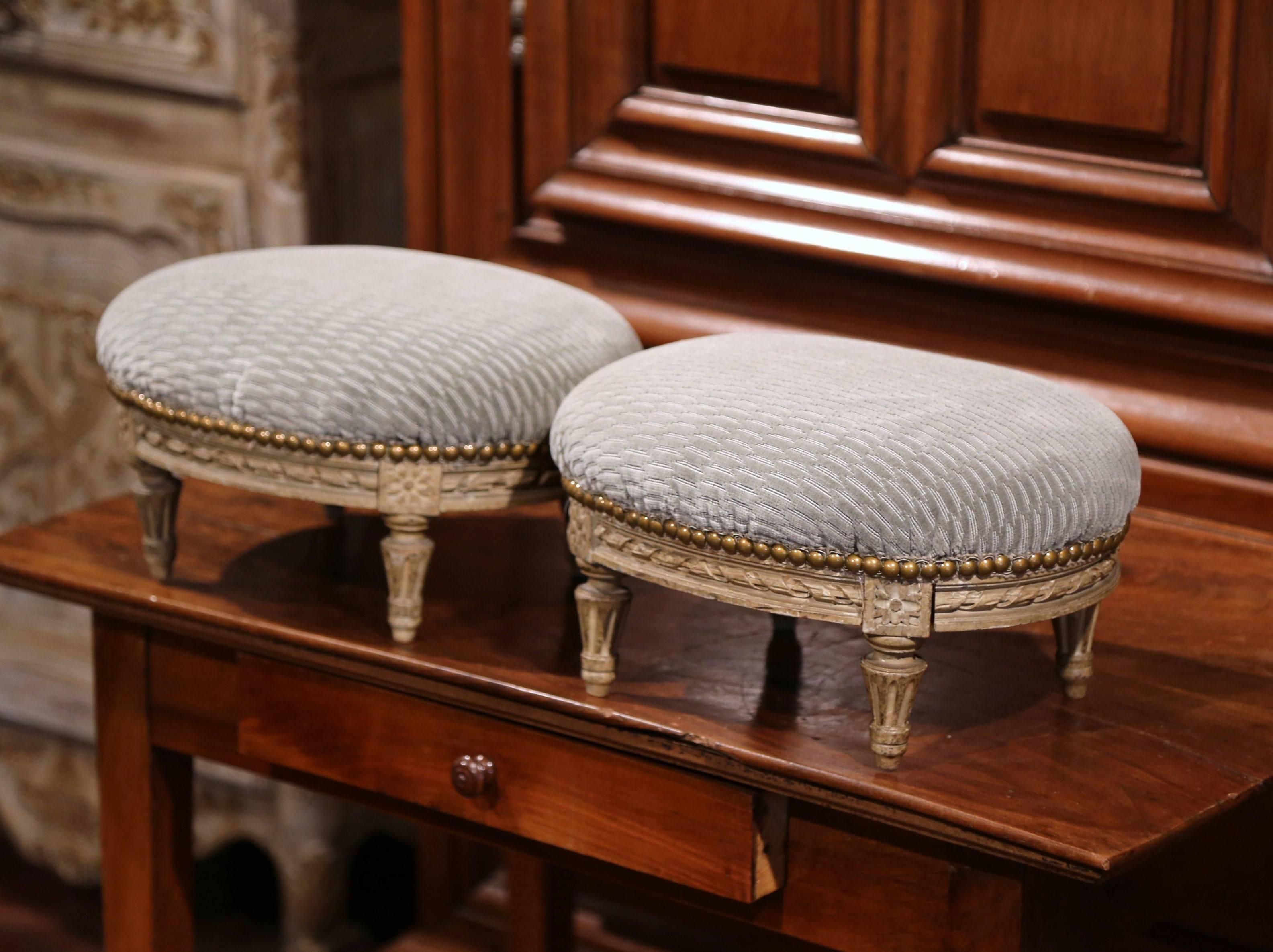 Elegant pair of antique footstools from Paris, France; crafted circa 1870, each oval stool features wonderful carving including carved medallions and tapered legs. They have the original painted finish and have been reupholstered with a blue velvet