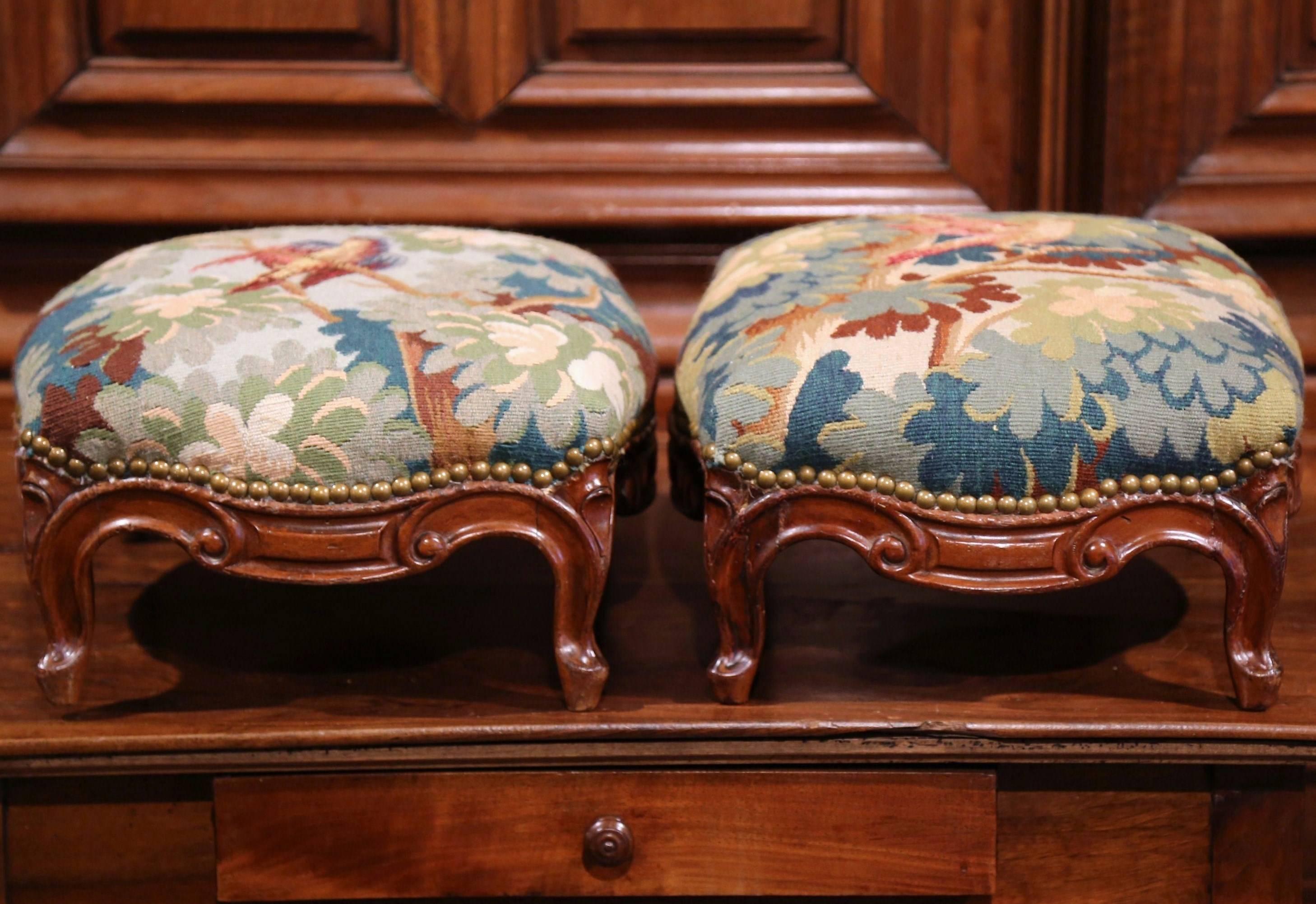Incorporate neoclassical beauty into your home with this exquisite pair of colorful Louis XV footstools. Crafted in Lyon, France, circa 1870, these carved stools feature small scrolled feet over a scalloped apron; they are upholstered with antique