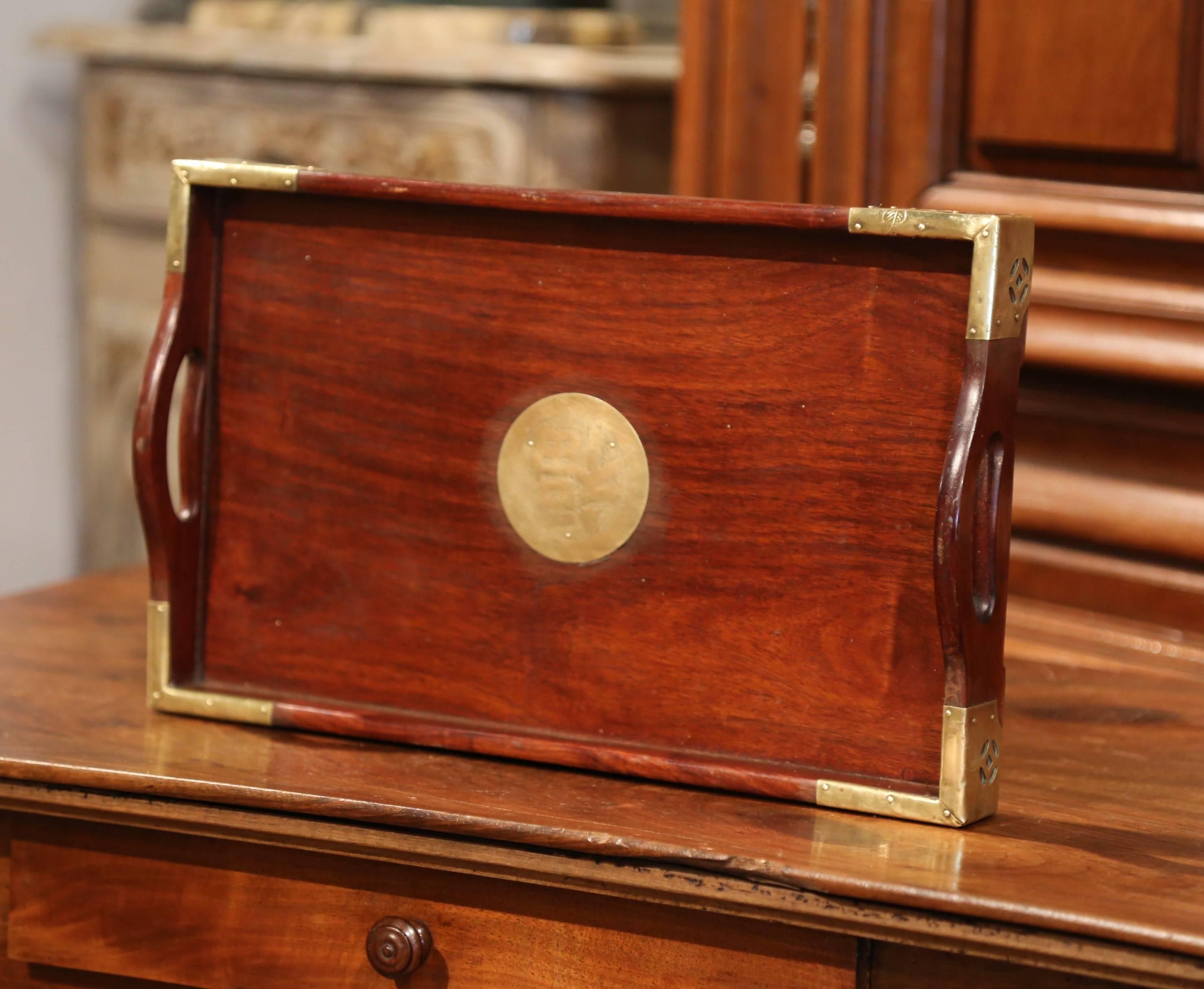 This beautiful rosewood tray with handles was crafted in China, circa 1960. The classic, rectangular tray features brass mounts with engravings in each corner and a round, embellished center medallion with engraved motifs. The tray is in excellent