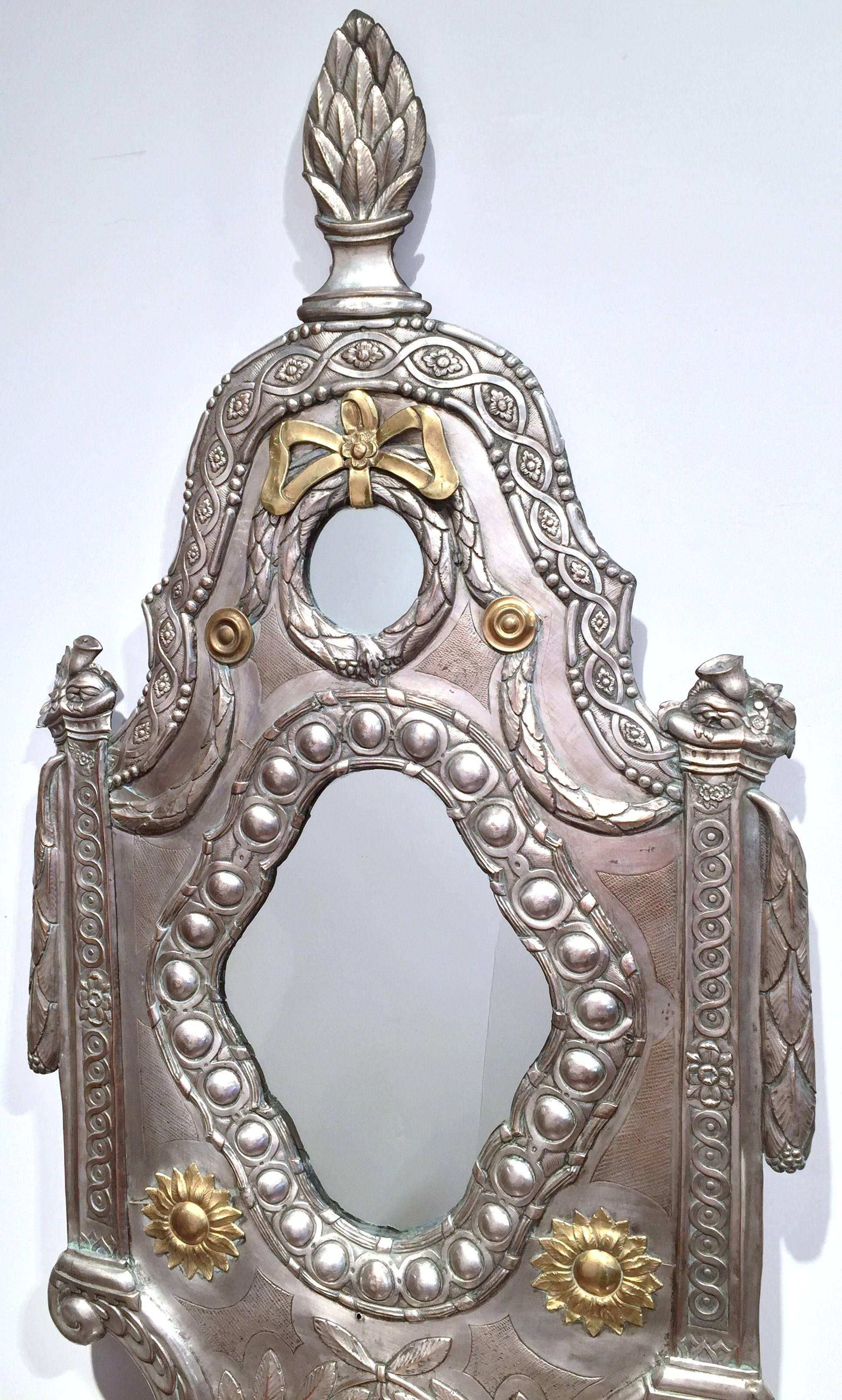 This unusual antique copper and silver plated mirror was crafted in France, circa 1840. The overlay wall hanging piece features some repousse decor, including large cones on top and bottom, three shaped mirrors, draped swags on both sides, and the