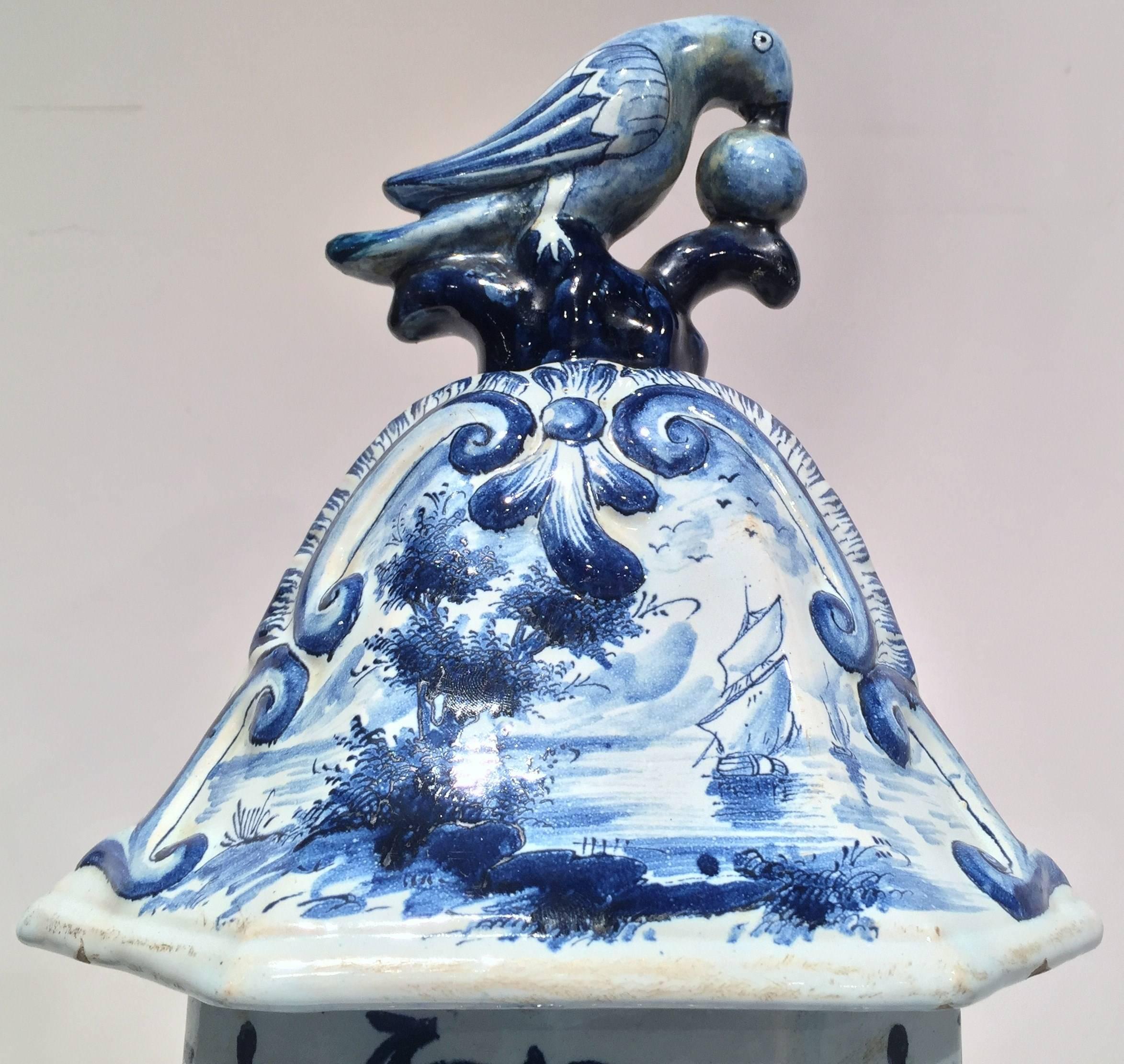 Large elegant blue and white Delft vase depicting a romantic scene of a courting couple (circa: 1900). The shoulders and base of the vase are decorated with diamonds. The cover has a traditional parrot pecking the ball finial. Large 