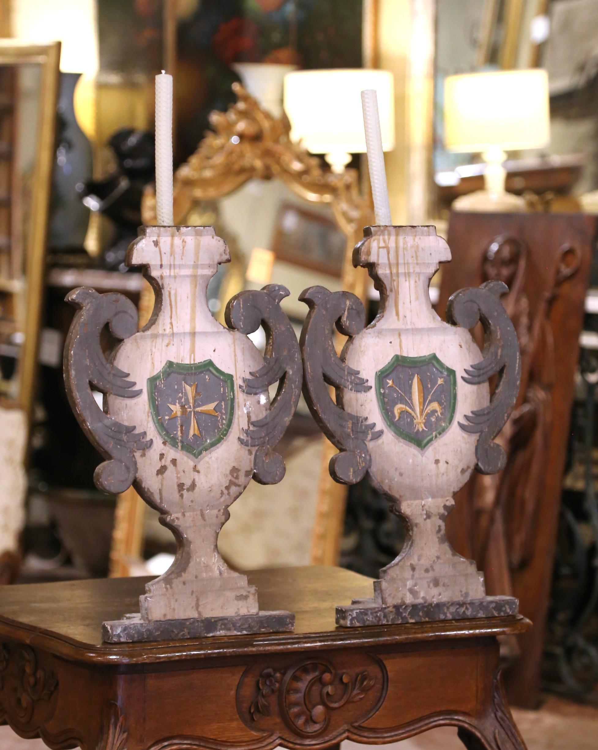 Aggiungi un tocco di fascino ecclesiastico al tuo arredamento con questa straordinaria coppia di candelabri antichi. Intagliato a mano in Italia intorno al 1860, ogni candeliere in legno ha la forma di un'urna stilizzata con manici a voluta,