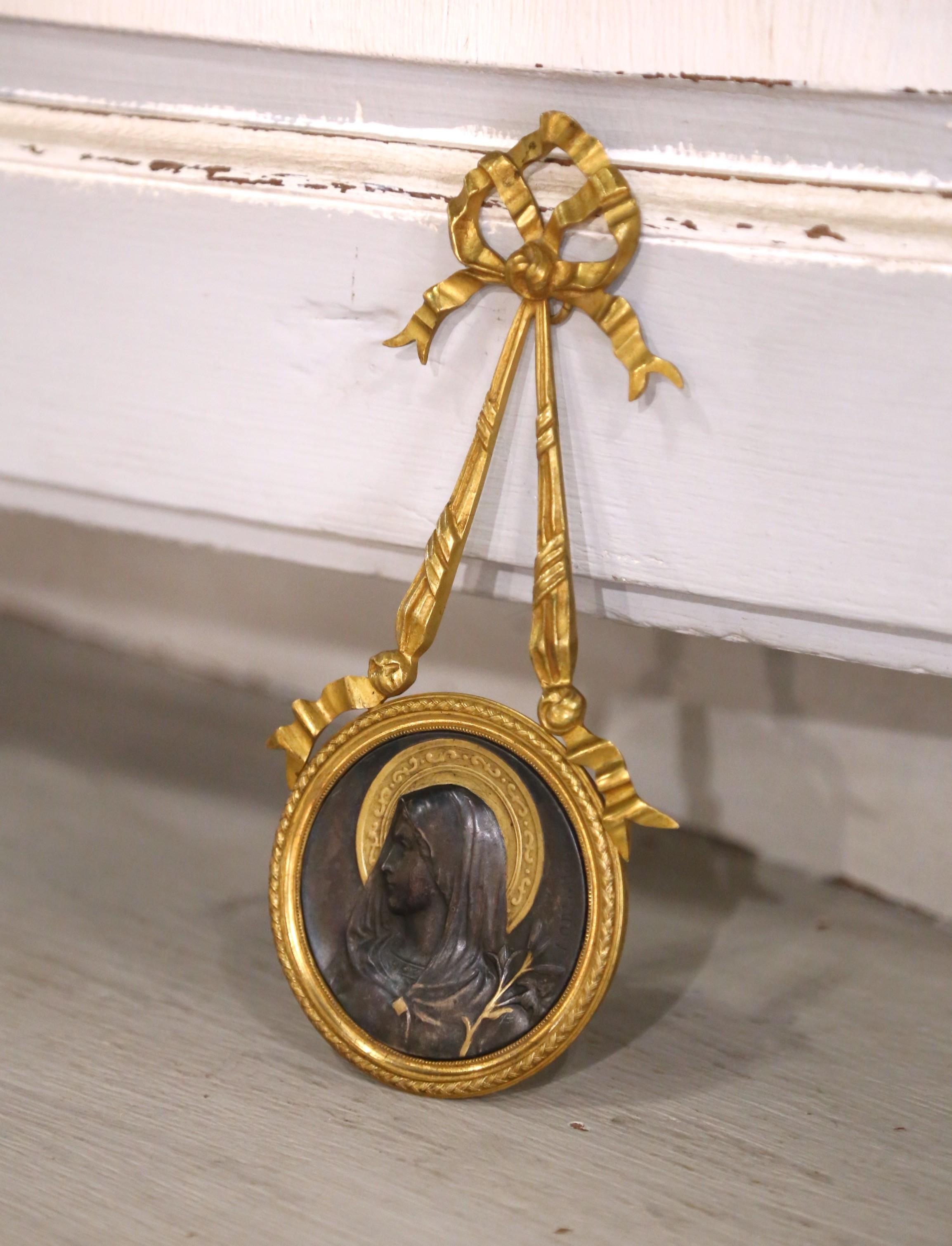 Ce médaillon de dévotion raffiné a été coulé en France vers 1870 et présente un profil finement sculpté de la Vierge Marie en bronze patiné. Son visage serein est encadré d'une auréole dorée et rehaussé d'une branche d'olivier délicatement dessinée,