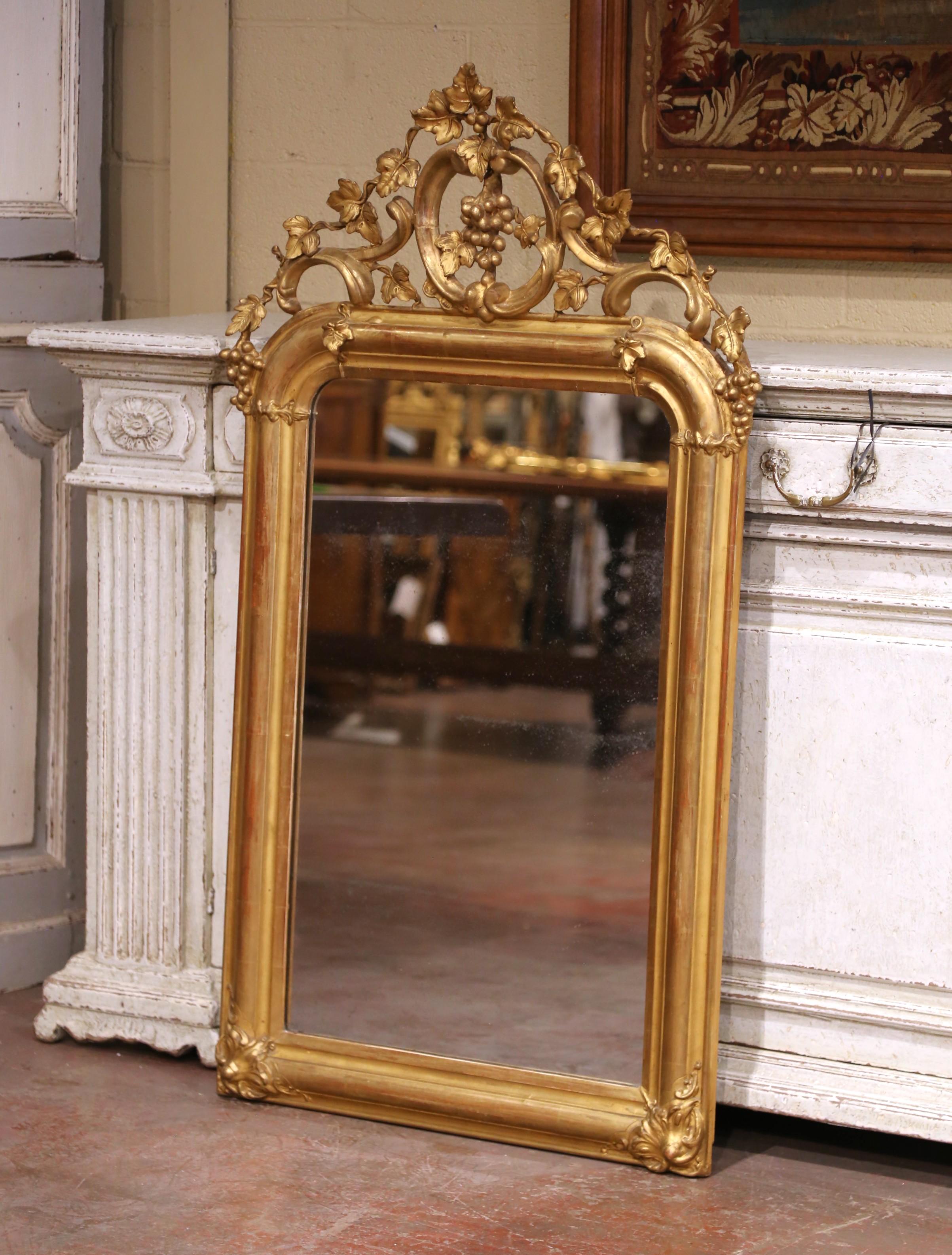Decora un tocador, una bodega o la entrada con este elegante espejo dorado francés del siglo XIX. Fabricado hacia 1870, el marco de estilo Luis XV presenta un frontón ricamente tallado y perforado, adornado con enredaderas, racimos de uvas y