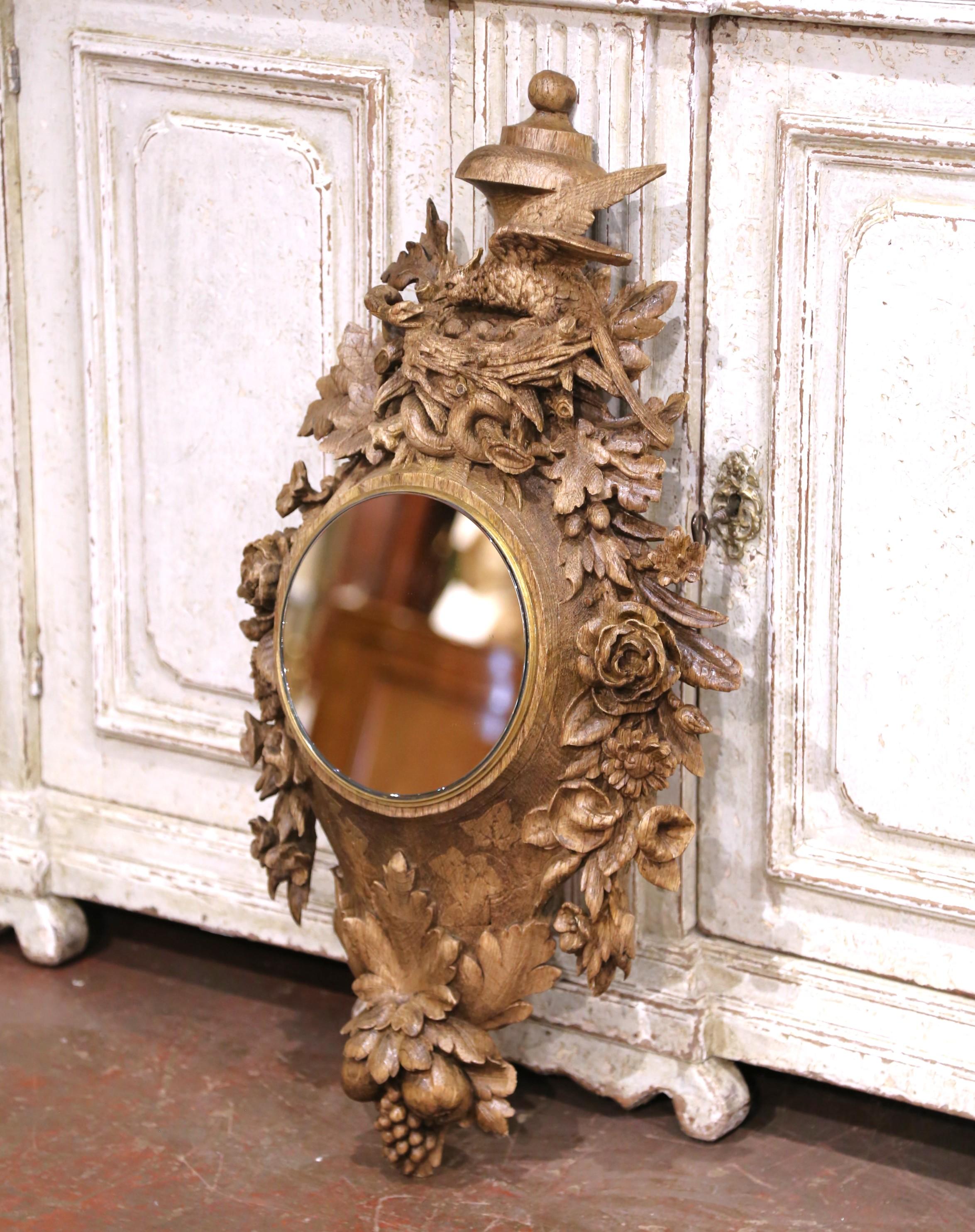 A striking example of French Black Forest craftsmanship, this intricately carved mirror was created circa 1870 and is made of stripped oak with a light, natural patina. The circular mirror from later addition is framed in finely cast bronze trim,