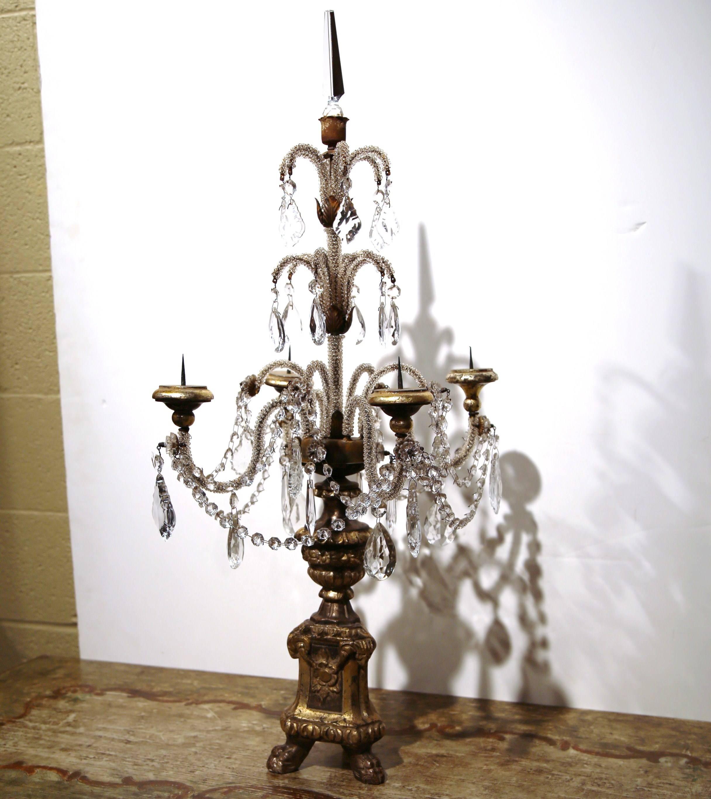 This delicate pair of candelabras was created in Italy, circa 1920. The elegant candle holders each have four arms with crystal and cut-glass pendants, gold leaf finish on the giltwood carved base with small feet, and a decorative glass finial to