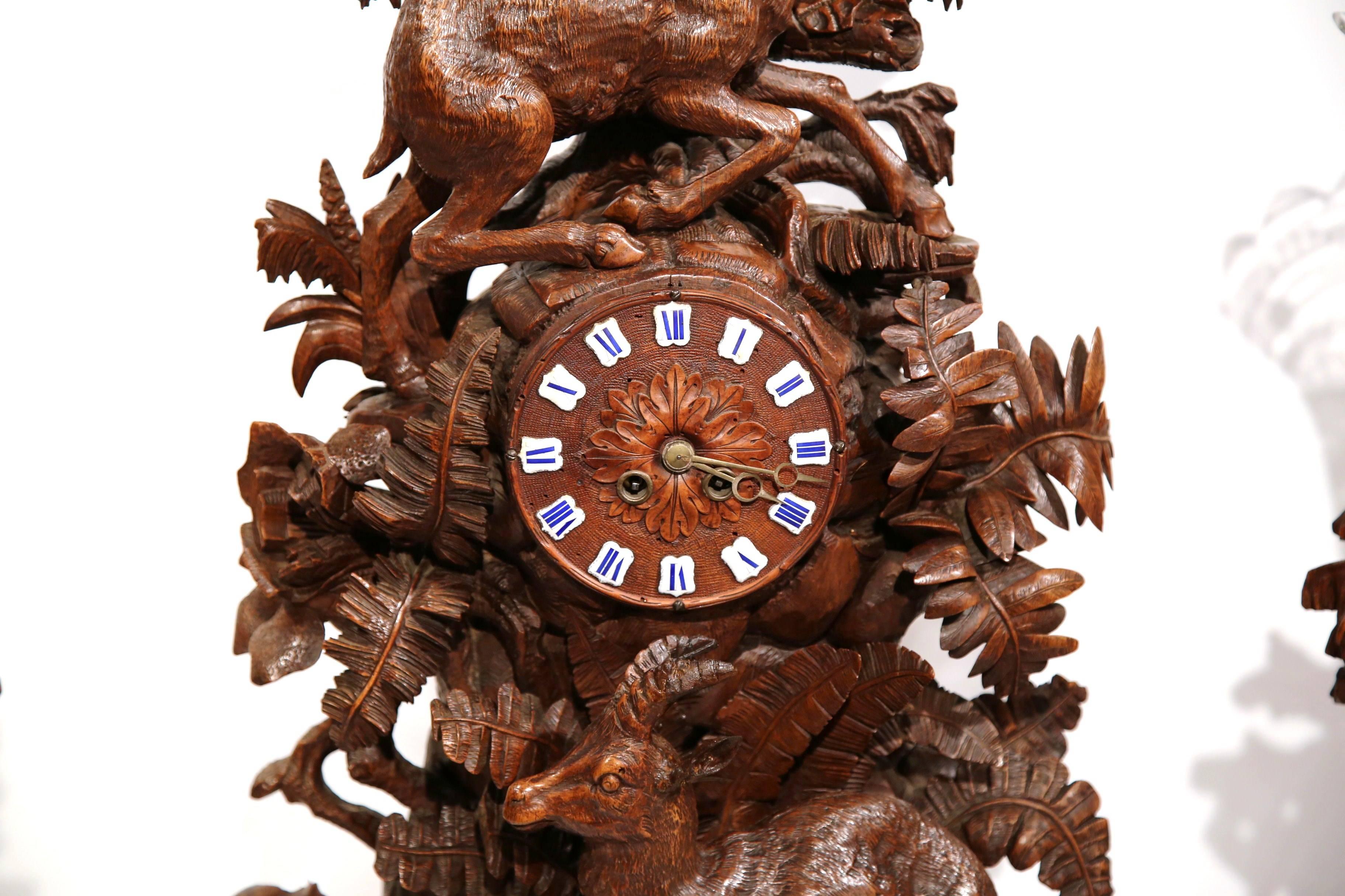This important antique three-piece mantel clock set was crafted in Switzerland, circa 1860. The impressive, hand carved fruitwood clock features a deer at the pediment above the round face clock and embellished with a resting chamois, trees, floral