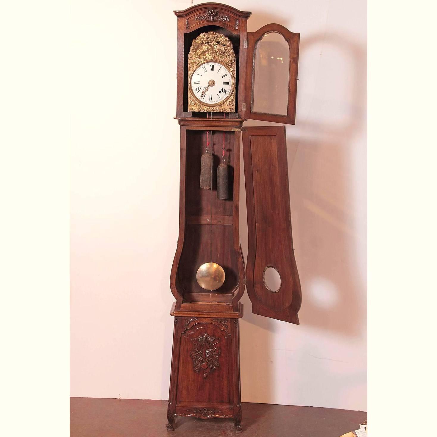 This beautiful long case clock was hand-carved in Avignon, France, circa 1880; the antique fruitwood piece sits on small cabriole feet and features all the typical carving attributes and motifs from Provence including farmer's tools, music