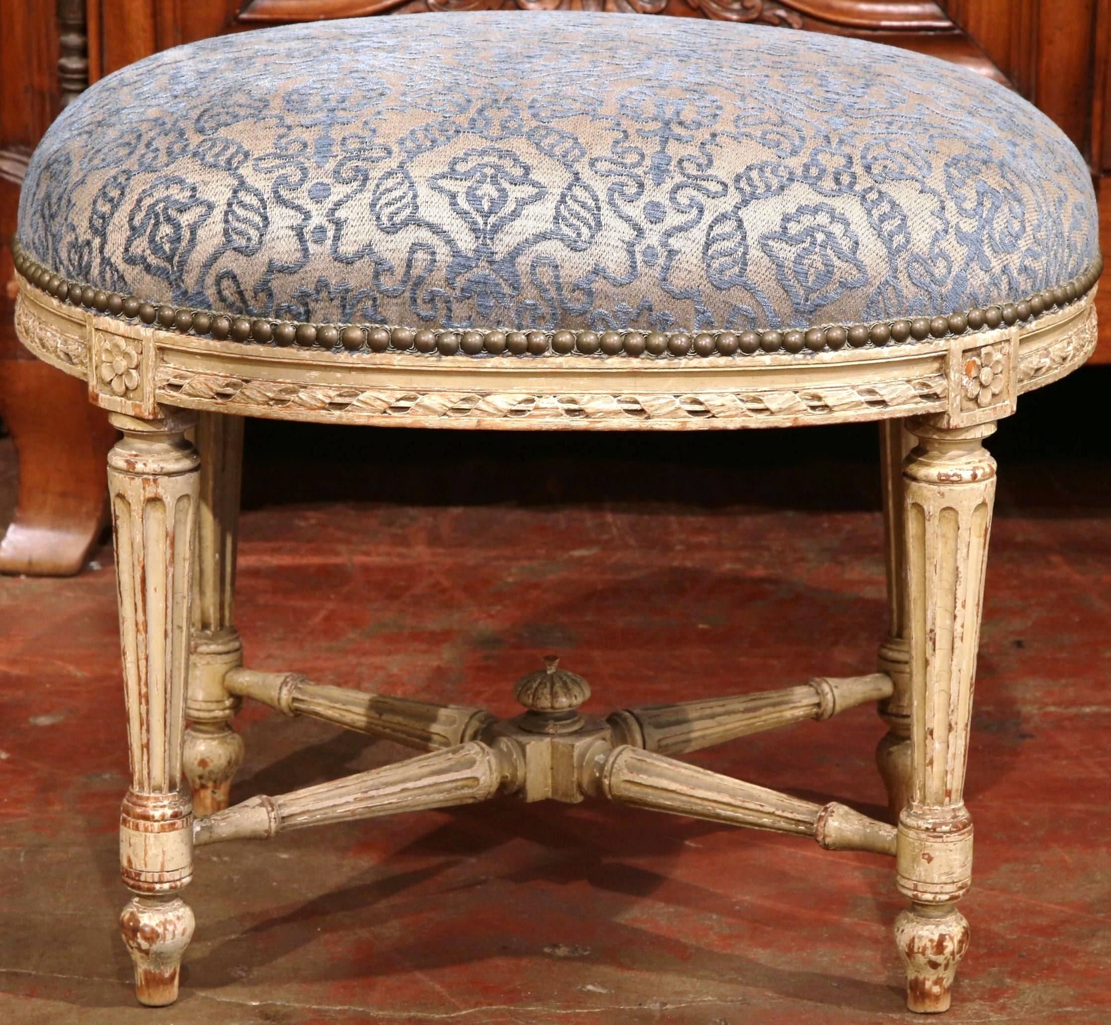 This elegant, antique beige painted stool was crafted in France, circa 1860. The oval seat has hand a frame with carved rosettes, fluted legs, and a bottom stretcher with a center wood finial. The stool features the original painted finish around