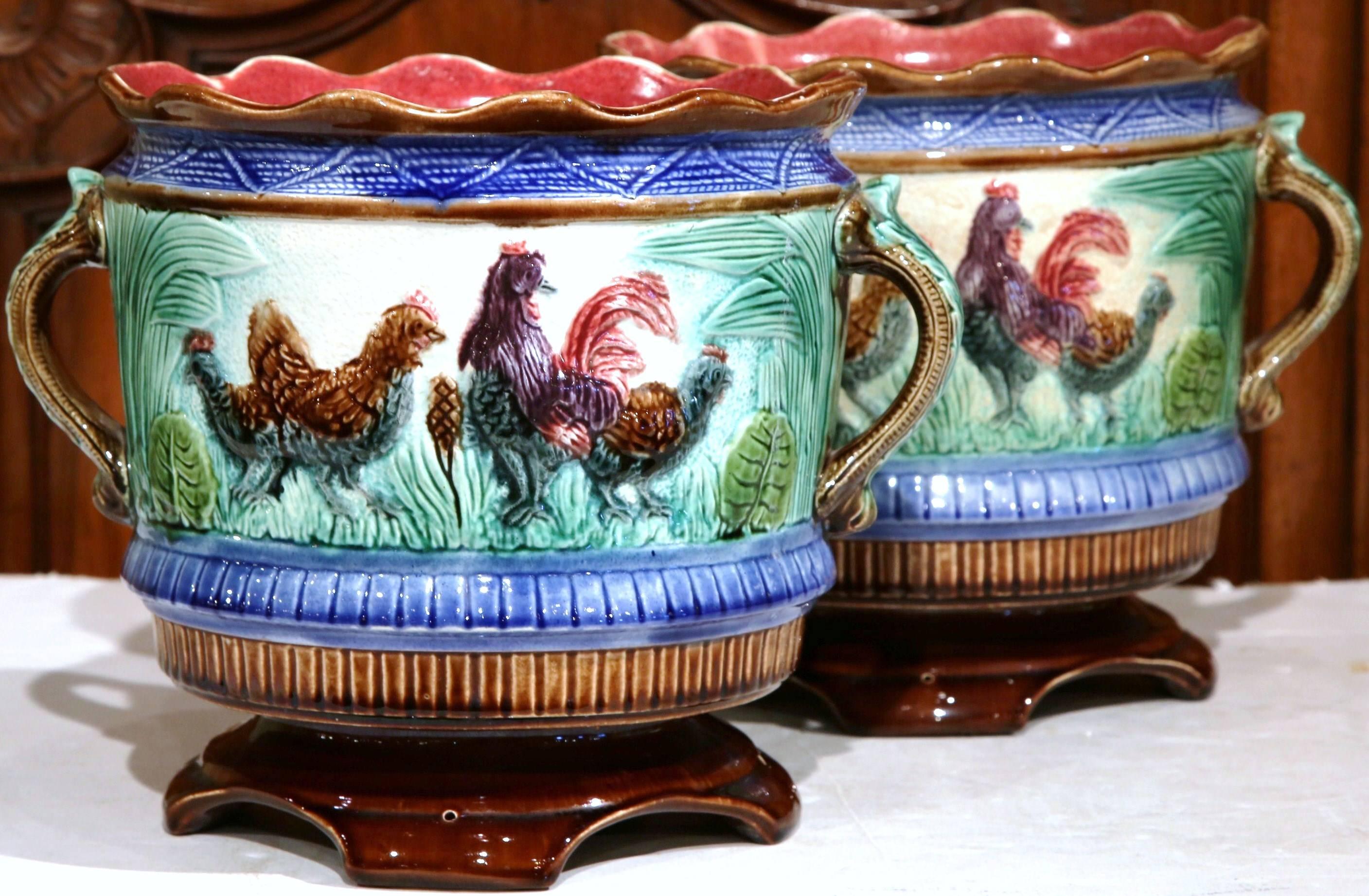 These Majolica jardinières were crafted in France, circa 1880. The colorful, antique pots have scalloped edges at the top, side handles, and sit on small, curved feet. Both of the painted cache pots are illustrated with a Classic, French country
