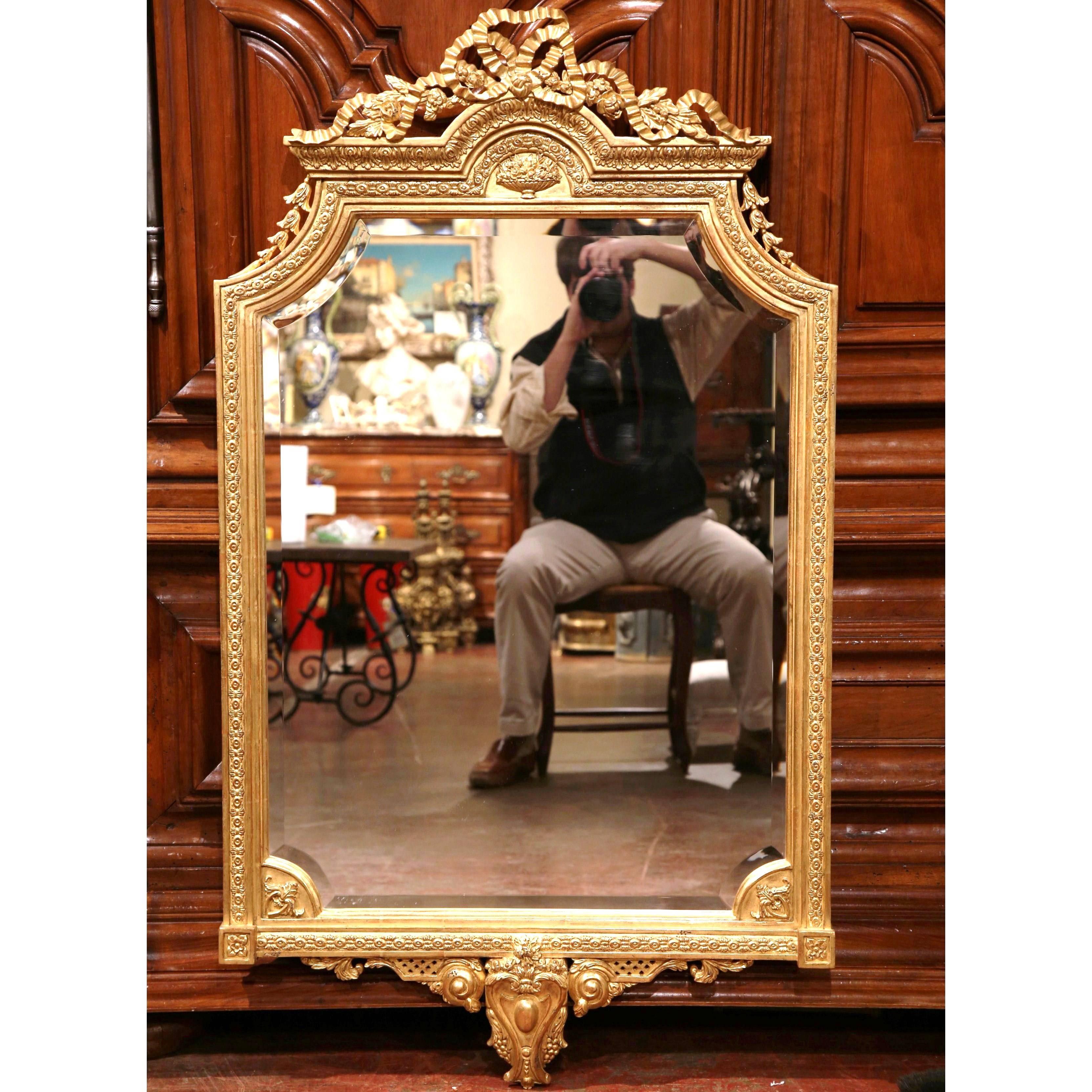 This pair of Louis XVI carved gilt mirrors from France, circa 1960, would make an elegant addition to any home. The unique wall mirrors feature beveled glass, a carved pediment with the traditional Louis XVI ribbon bow on top, and a carved cartouche