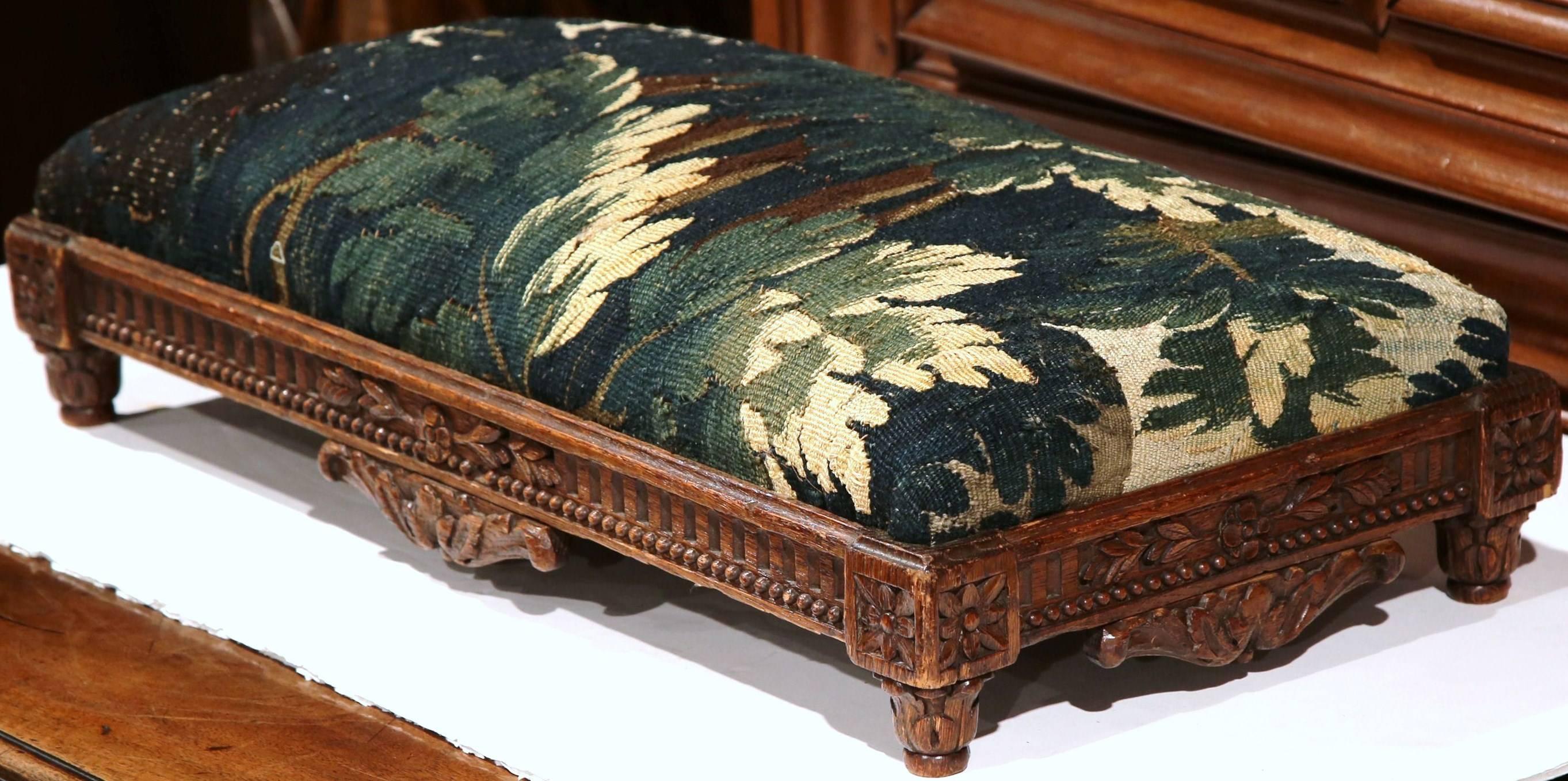 From its expertly carved base to its colorful upholstery, this long, antique foot stool would make a lovely addition to a formal living room. Crafted in France, circa 1830, the elegant oak stool with hand carved motifs around the frame, is