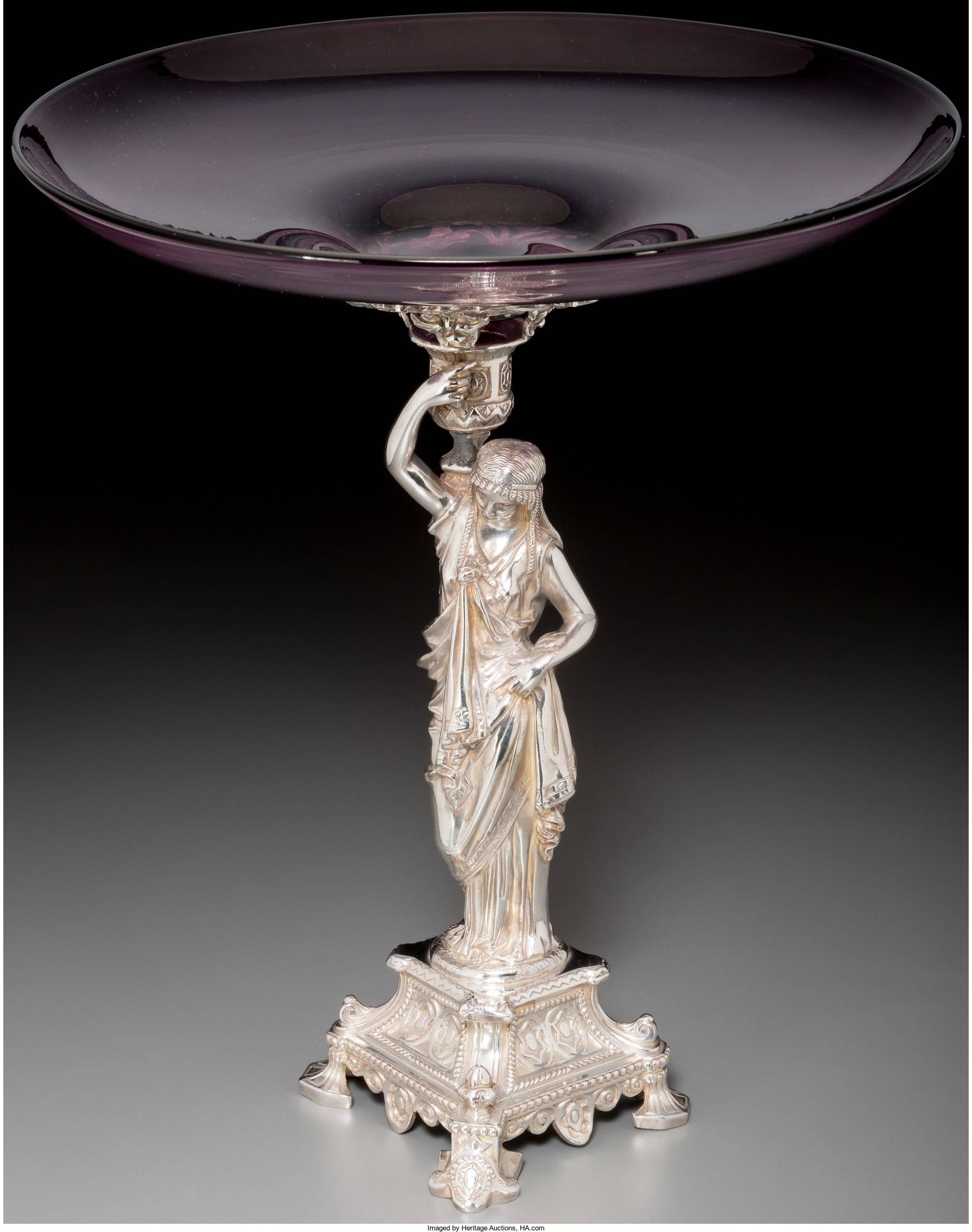 Decorate a table or buffet with this sophisticated silver plated center bowl. Crafted in England circa 1870, the antique centerpiece features a woman figure in Roman attire standing on a podium and holding a wide, shallow glass bowl. The Classic