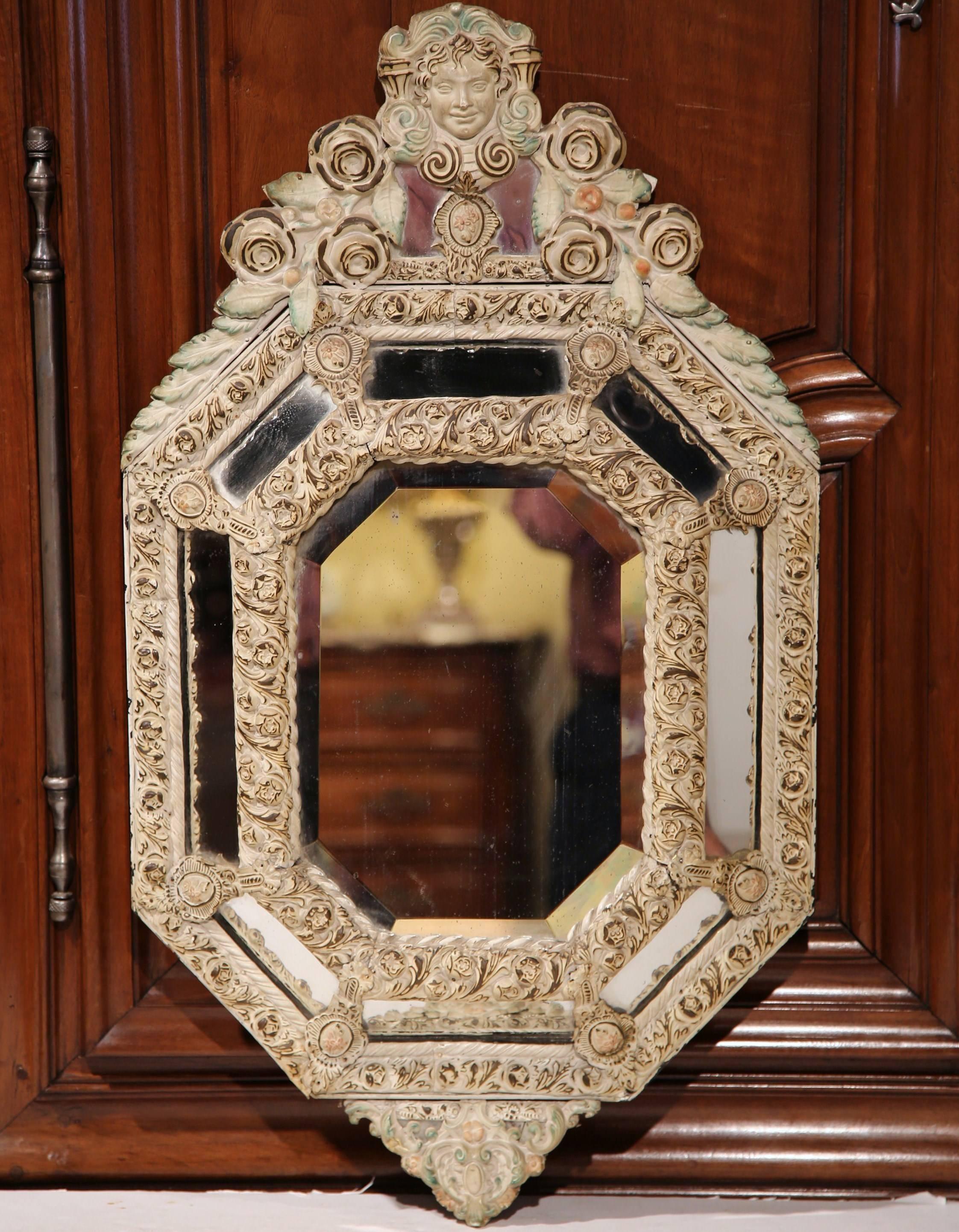 This elegant antique parclose mirror was crafted in France, circa 1860. Octagonal in shape, the beige painted repoussé tole mirror features a woman's face cartouche at the pediment, an intricate and raised frame with center beveled mercury glass,