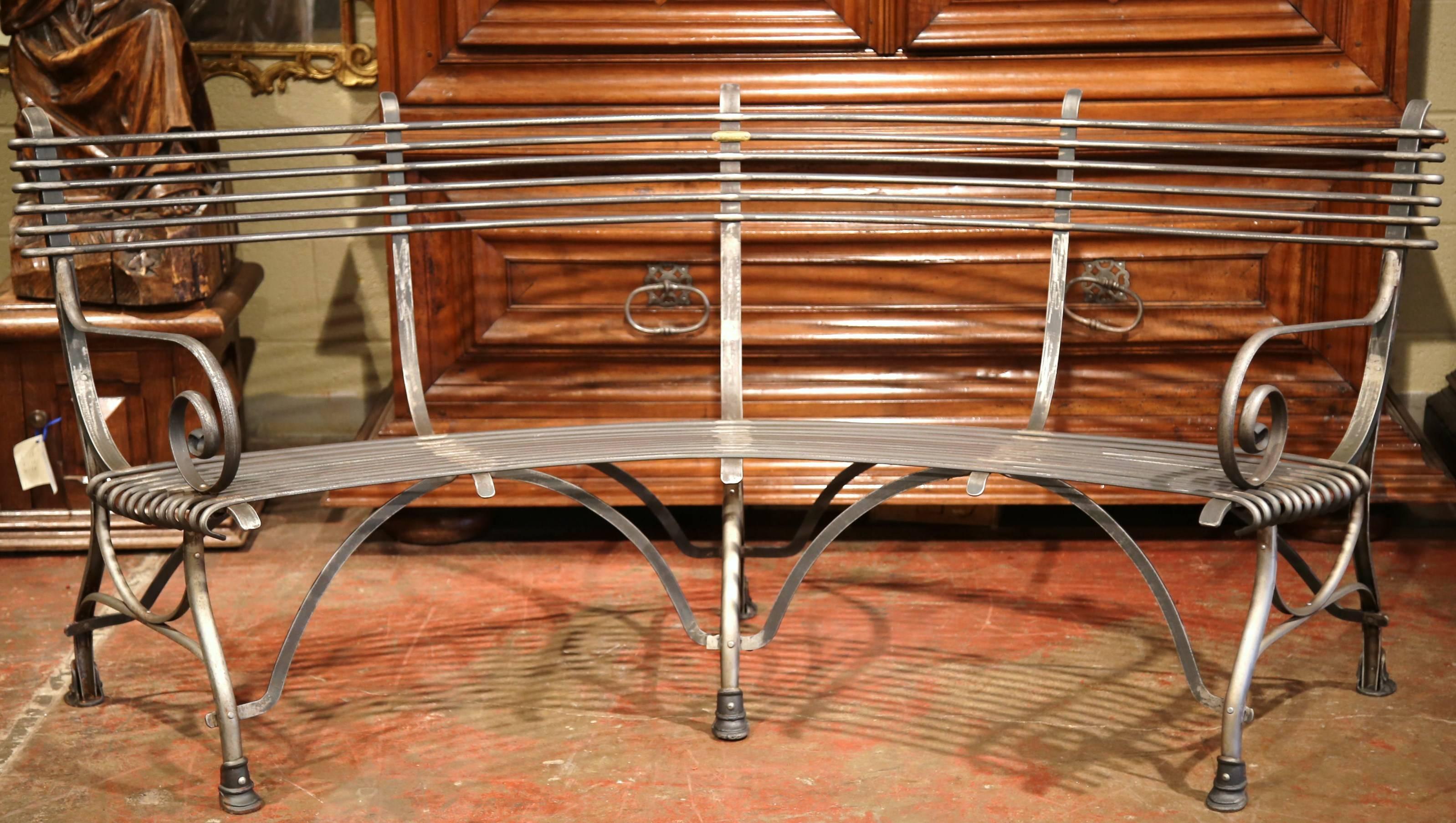 This elegant forged and curved iron bench was crafted in France and has a beautiful polished gun barrel finish. The rounded bench has gracious lines, scrolled armrests, a curved back and six hoof feet with stretchers. The bench is signed Sauveur a