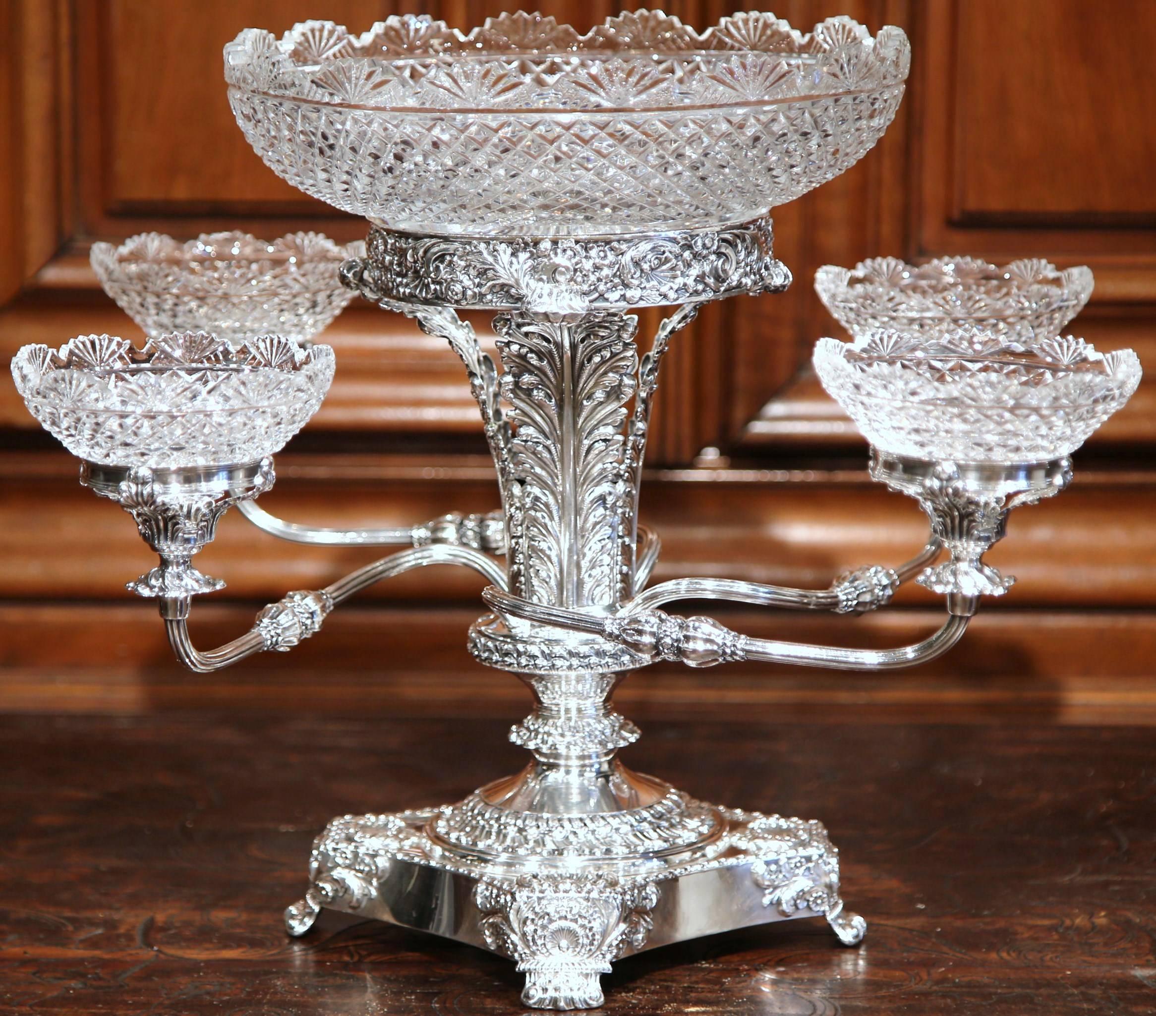 This elegant five-bowl antique epergne was crafted in England, circa 1880. The silverplated centrepiece features intricate floral decoration on the base, with a large cut-glass bowl in the centre and four scrolling arms supporting smaller cut-glass