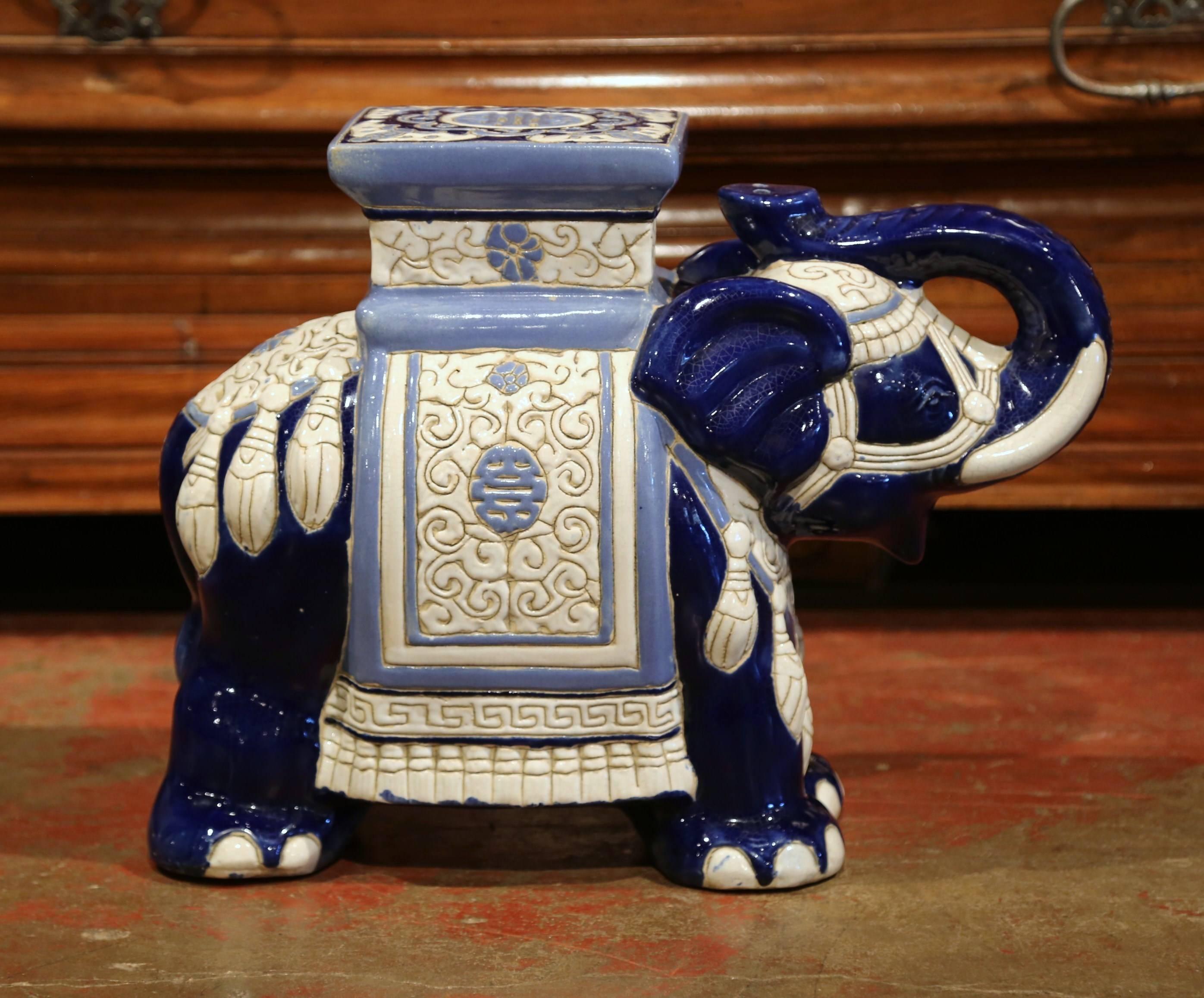 This interesting, porcelain garden seat was sculpted in France, circa 1950. The piece is in the shape of an elephant raising his trunk, which is heavily decorated in oriental finery. The mammal has a square seat at the top, and is hand-painted in a