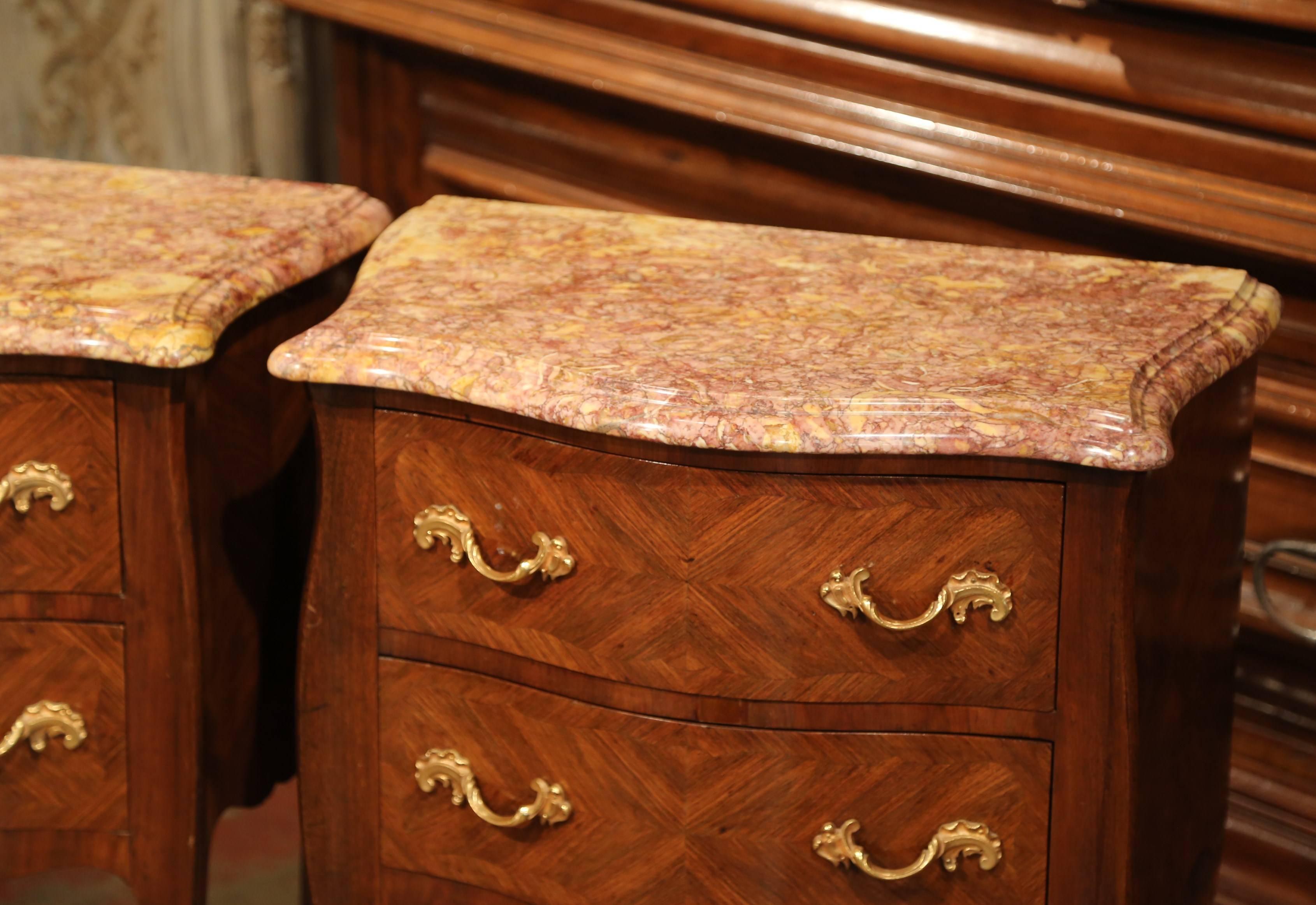 Complete your bedroom with this elegant pair of antique fruitwood chests. The small, bombe chest of drawers were crafted in Paris, France, circa 1920. Each chest has a beige marble top, marquetry work on all sides, two drawers across the front with