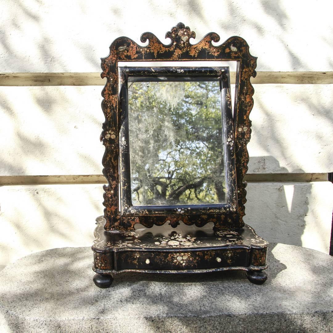 Continental black lacquered dressing mirror constructed of papier mache and wood with mother of pearl inlay and gilt decoration depicting classical motifs, 19th century. It is fitted with a tilting mirror and has a single drawer fitted in the lower