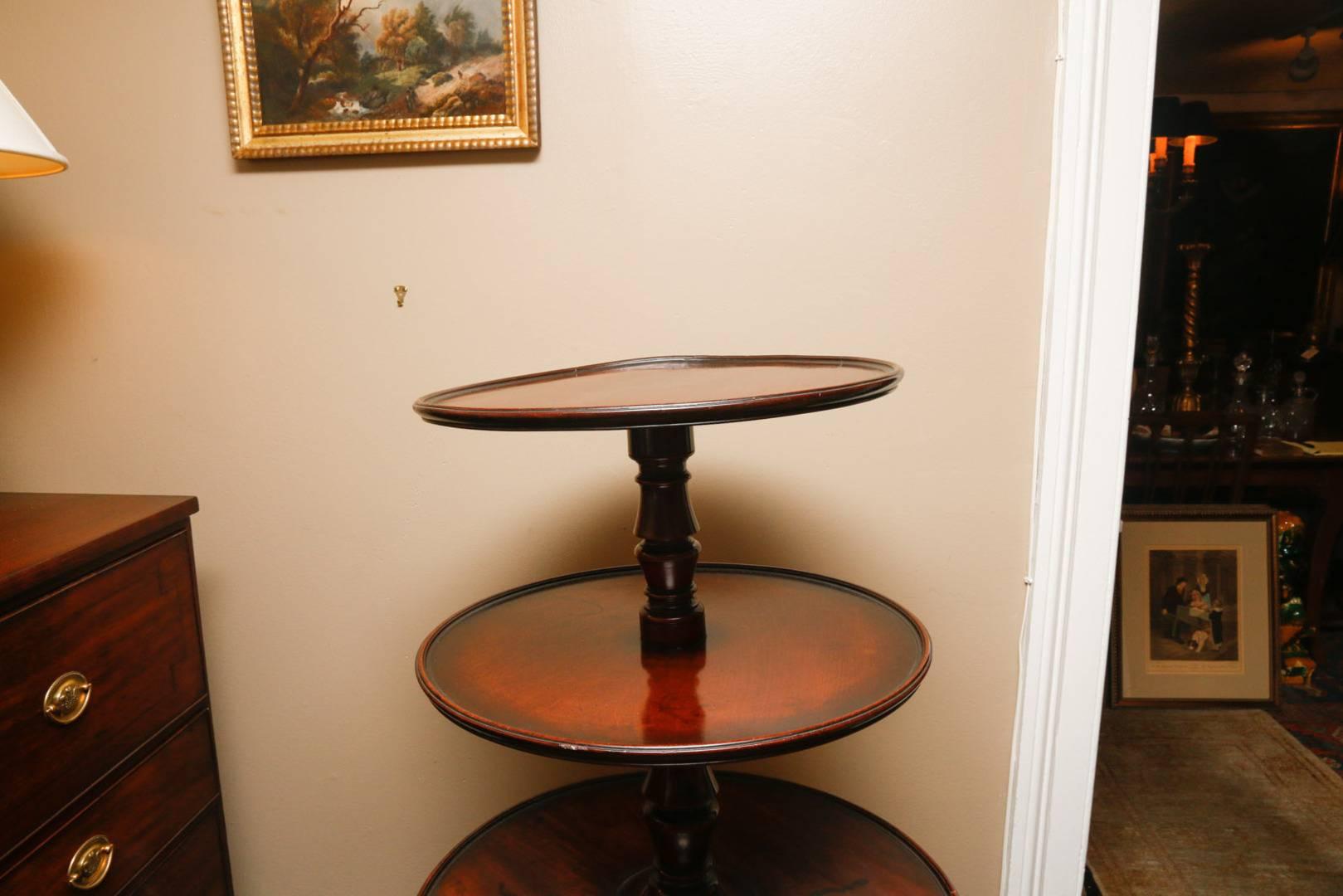 English Regency period (1811-1820) dumbwaiter in mahogany with three circular tiers supported by a central turned shaft and resting on three splayed legs ending in plain brass box caps with casters. The upper section measures 19 inches in diameter