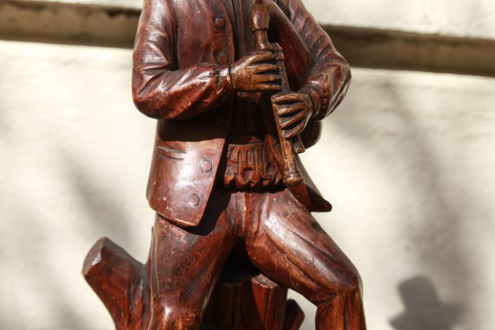 Pair of Dutch carved wooden figures that are mounted upon carved bases, 19th century. The figure of the gentleman can be seen sitting atop a stump and joyously playing his bagpipe. He is wonderfully detailed all the way down to his carved wooden