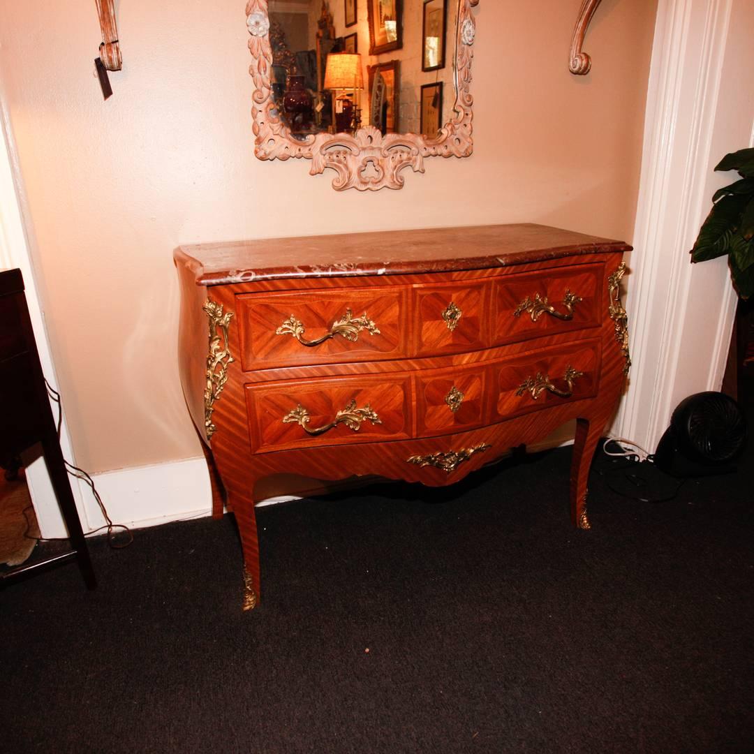 Louis XV style parquetry inlaid commode in a bombe form with two conforming drawers, cast gilt bronze hardware, and a rouge color shaped marble top. Late 19th to very early 20th century.
     